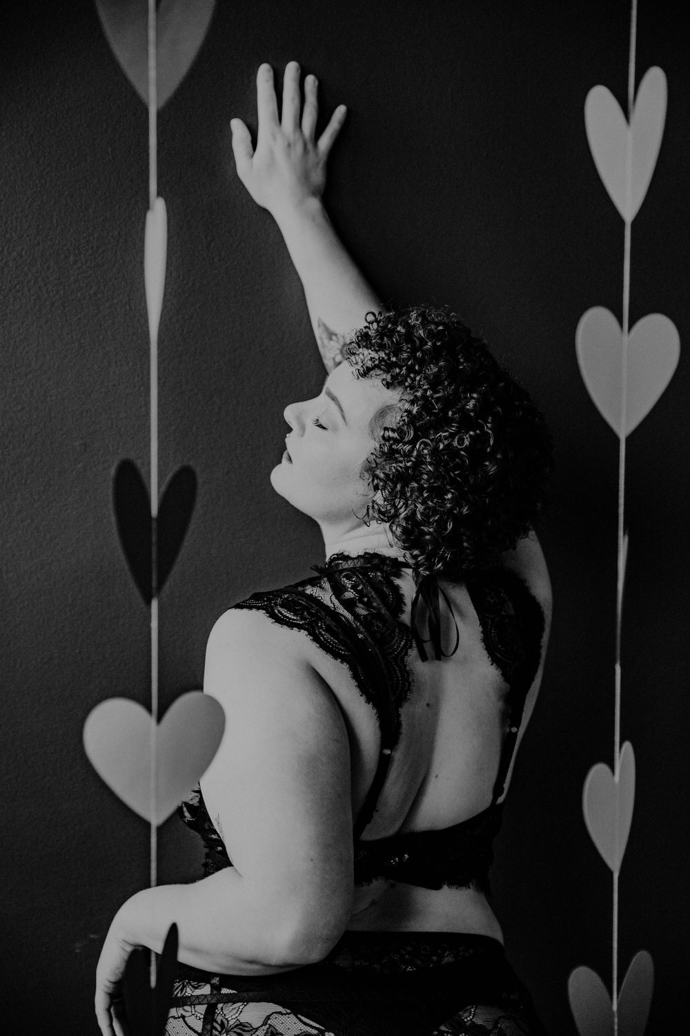 Artistic black and white photo of person reaching up toward hanging heart decorations.