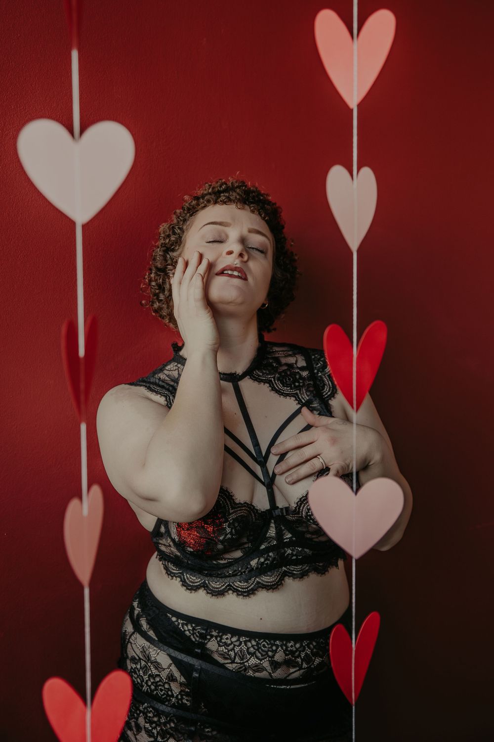 Portrait against red wall with heart decorations showing joyful expression.