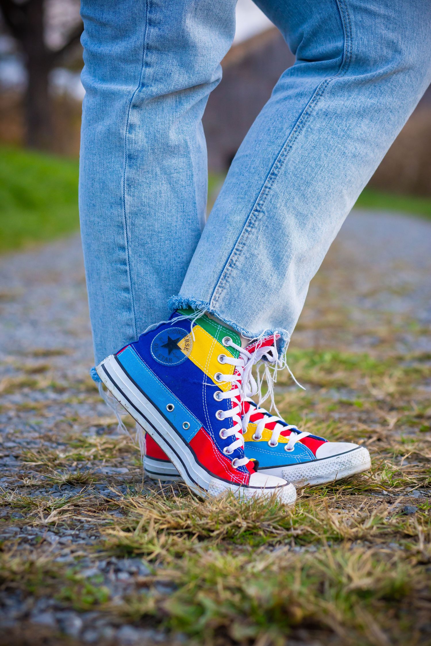 Colorful rainbow Converse sneaker with blue jeans on a wet path.