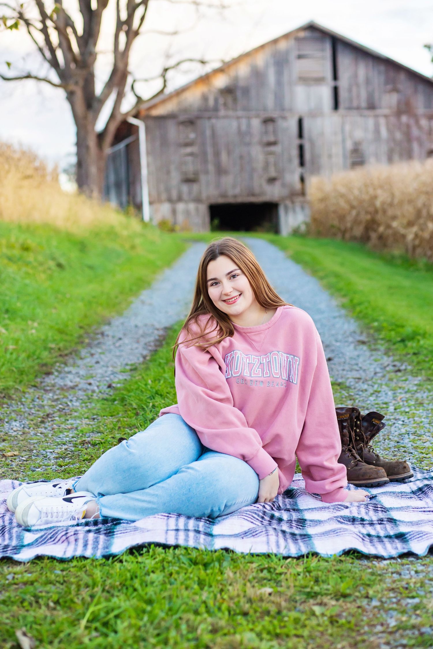 Person in pink sweatshirt relaxing on plaid blanket with rustic barn in background.