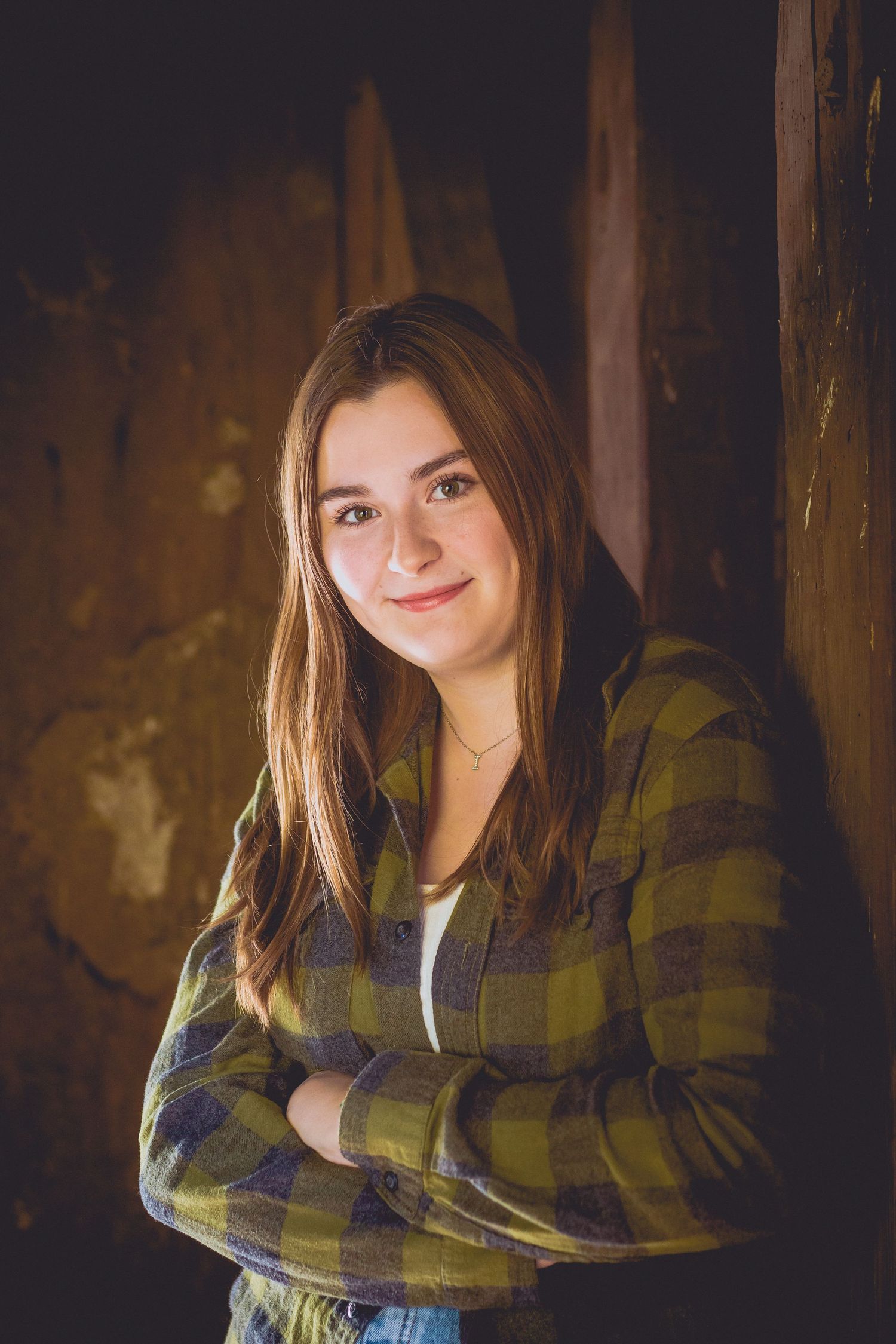 A portrait of someone in a plaid flannel jacket against a dark rustic background.