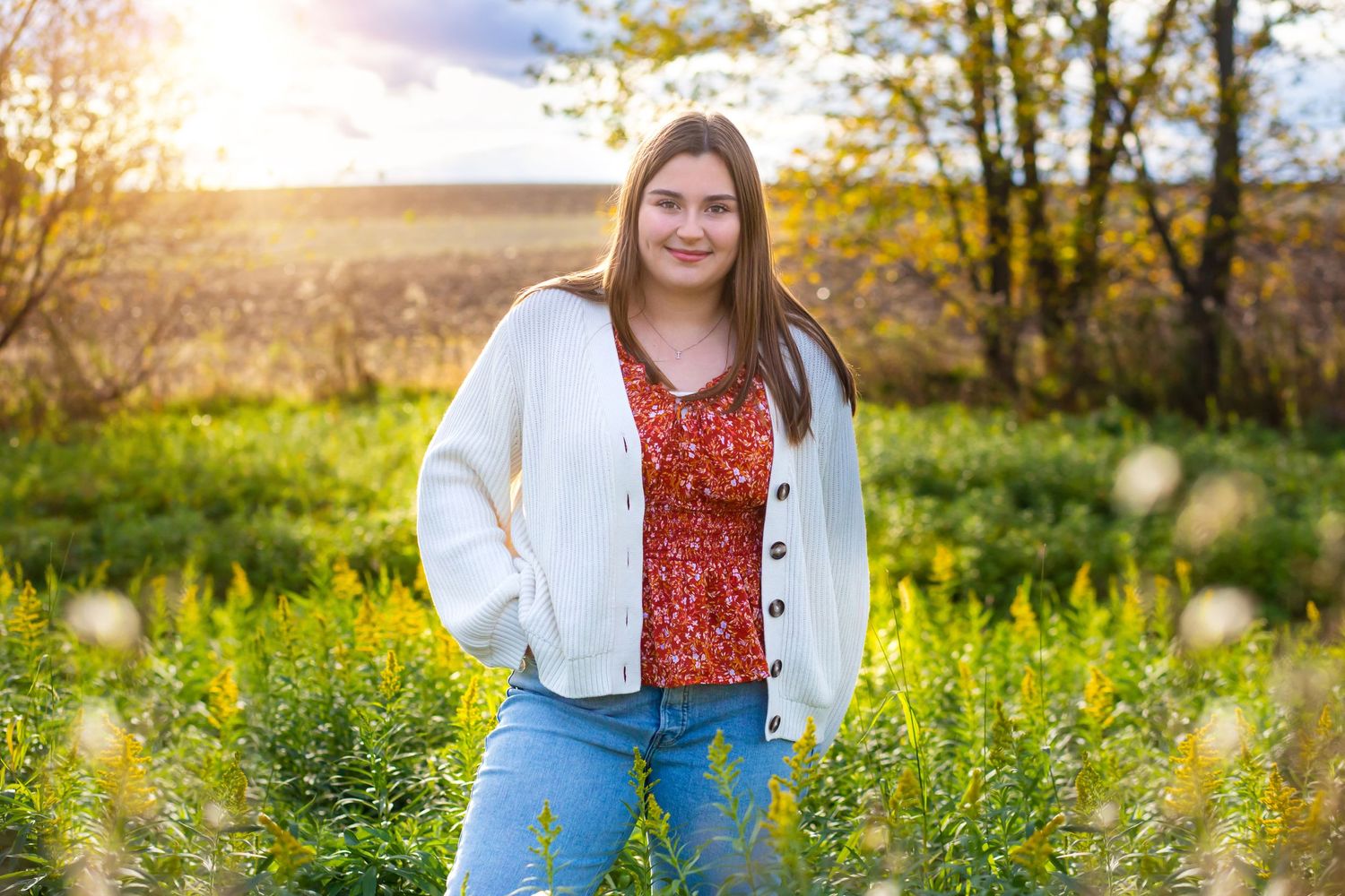 Person stands in a wildflower field at sunset wearing a red top and white cardigan.