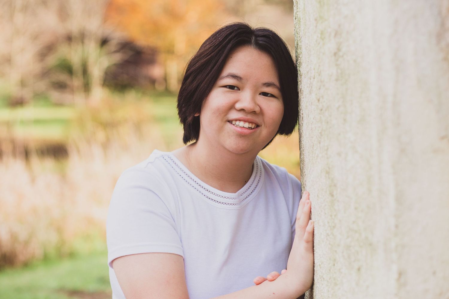 A person leaning against a light colored wall outdoors with a cheerful expression.