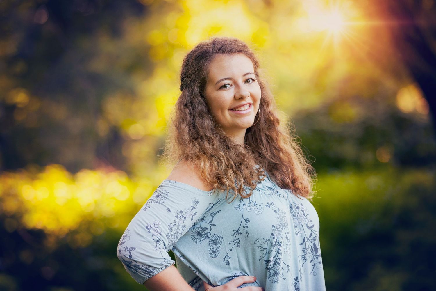 Portrait of woman in blue top against golden bokeh background in nature setting.