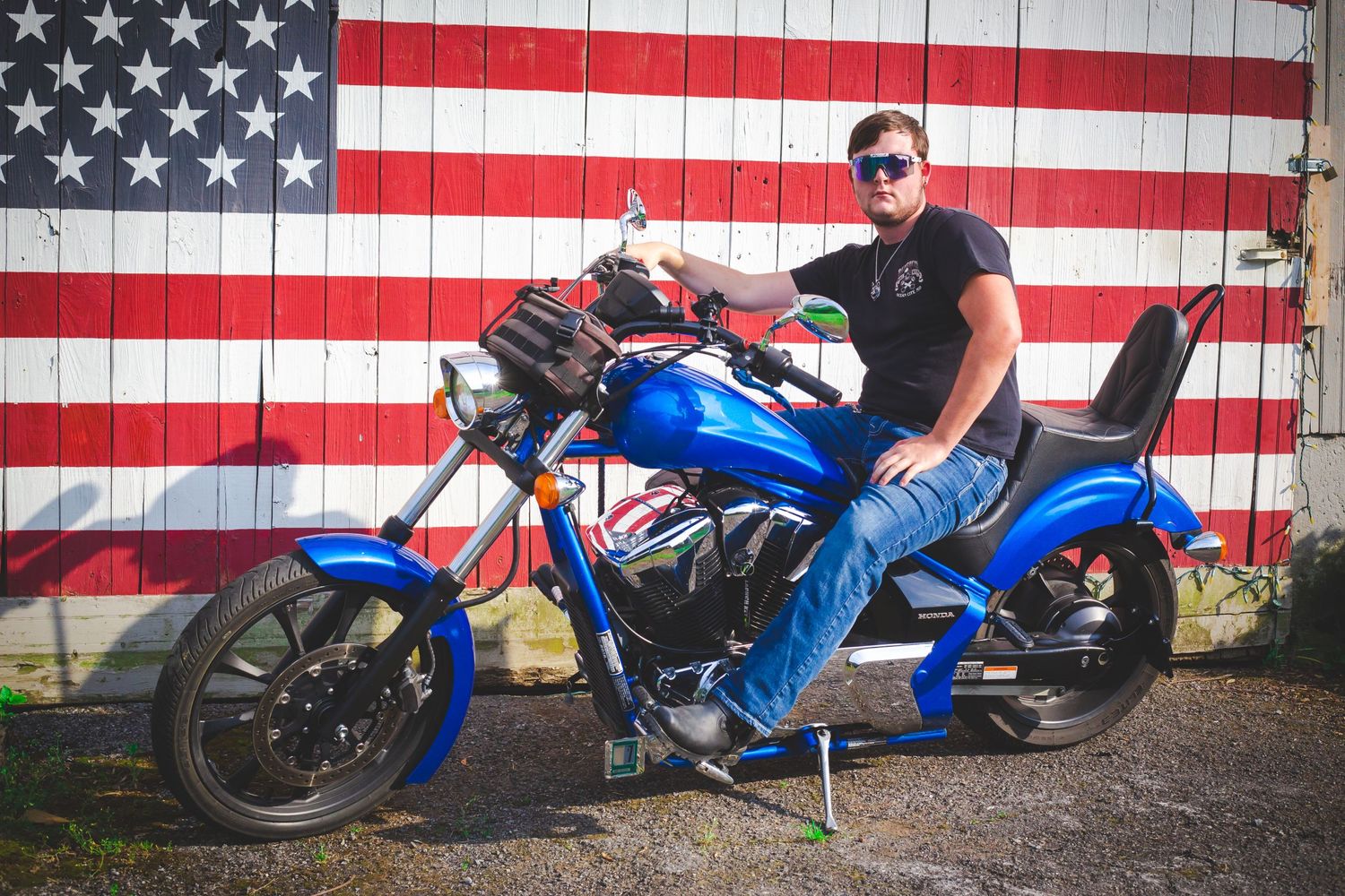 Person on blue motorcycle posed in front of American flag backdrop.