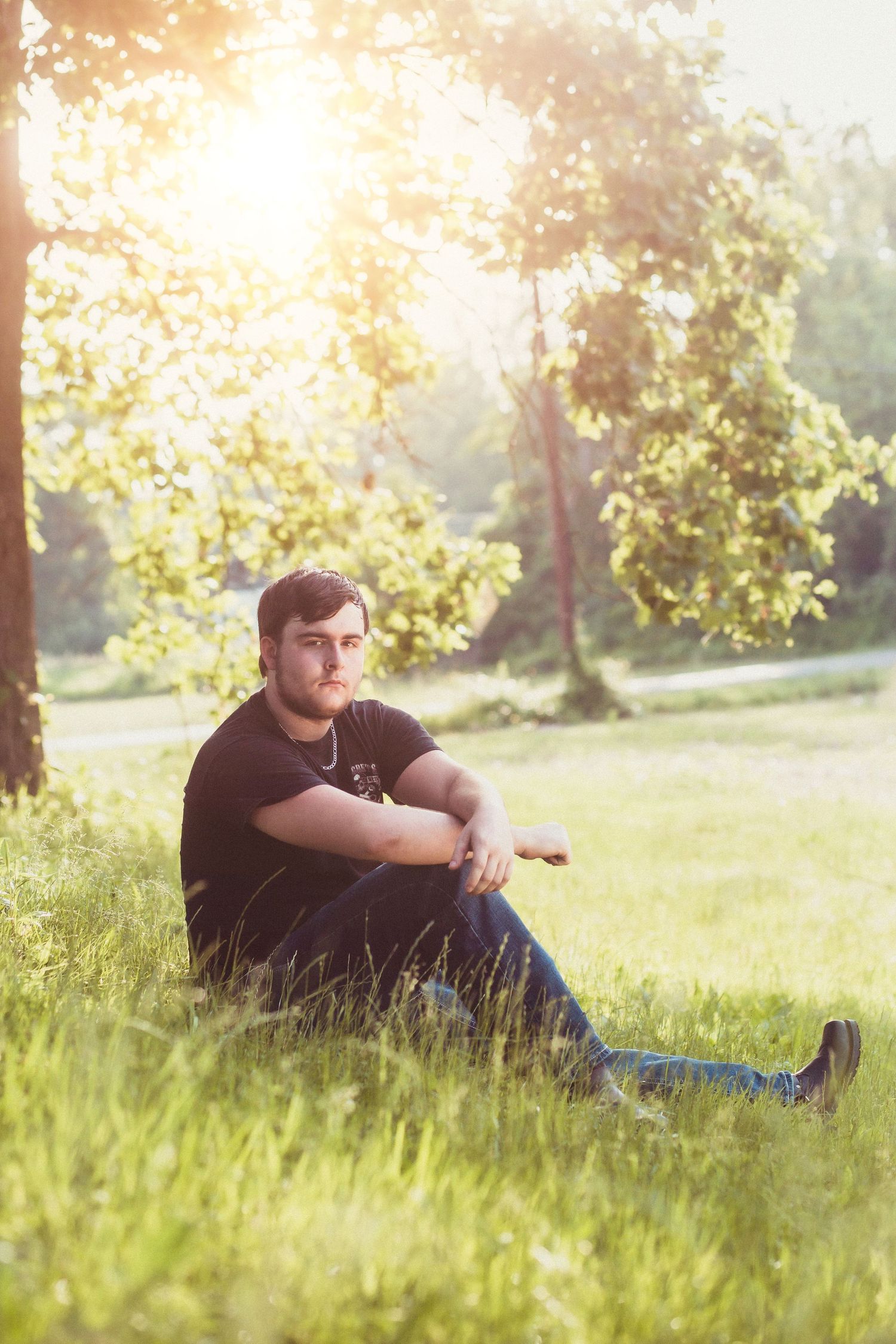 Person in black shirt sitting in sunlit grassy field at golden hour.