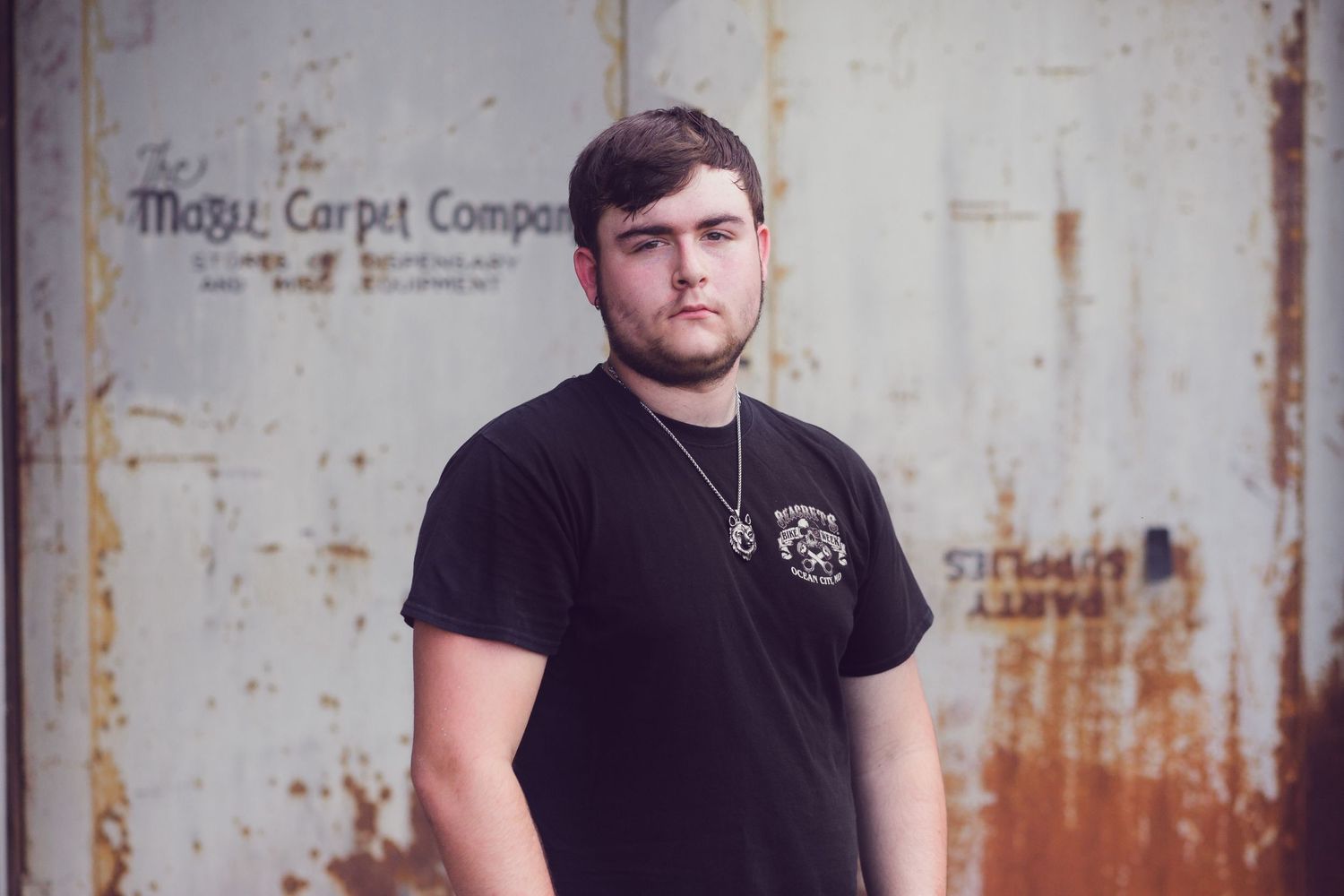 Person in black t-shirt posed against weathered metal wall.