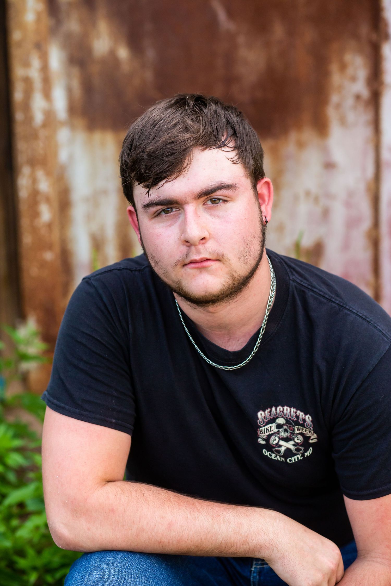 Person wearing black t-shirt with embroidered logo against rustic metal background.