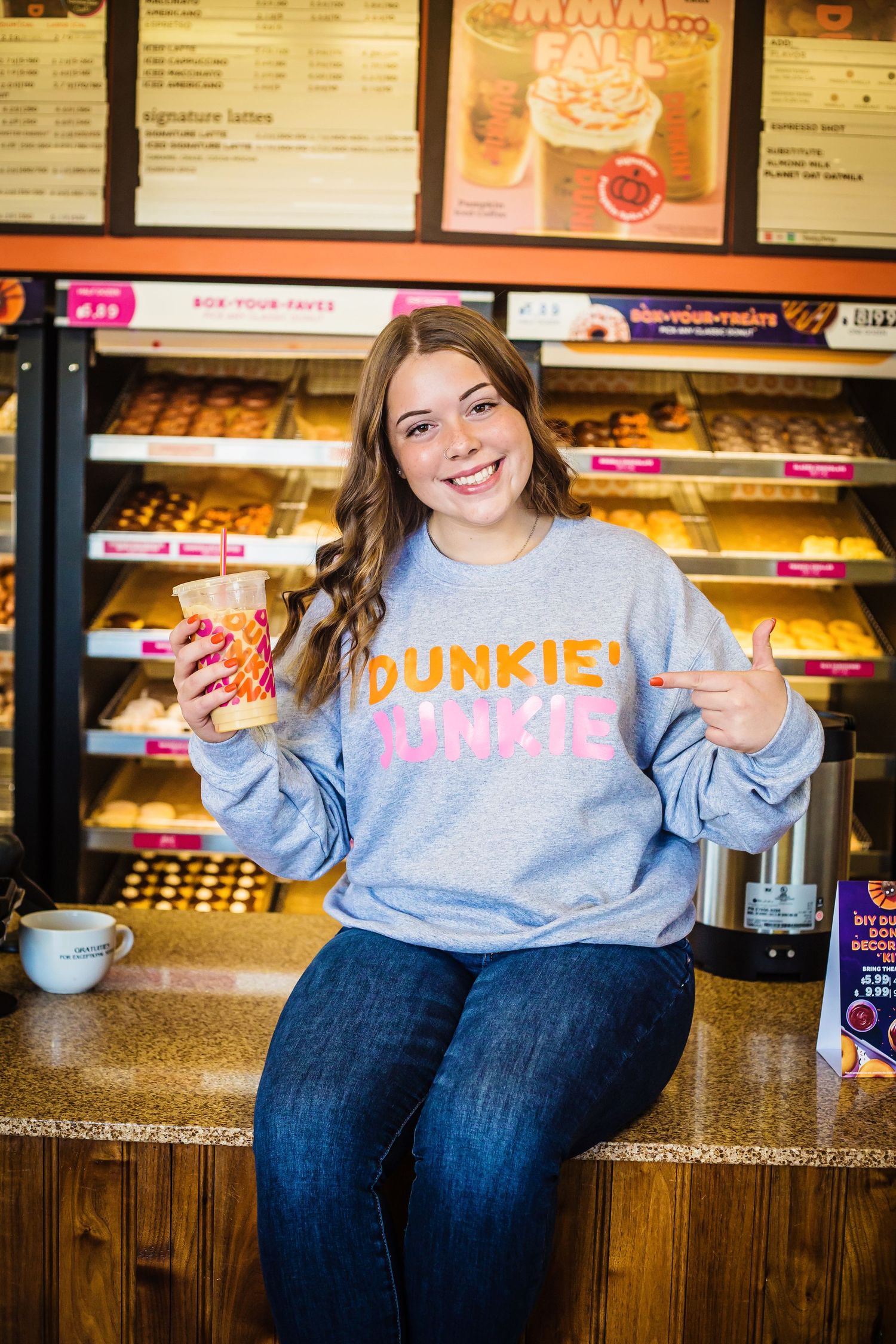 A casual portrait at Dunkin Donuts showing someone in a gray sweatshirt holding a drink.