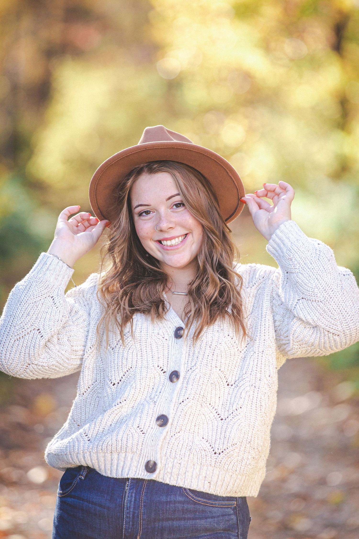 A fall portrait outdoors wearing a cream knit cardigan and brown hat.