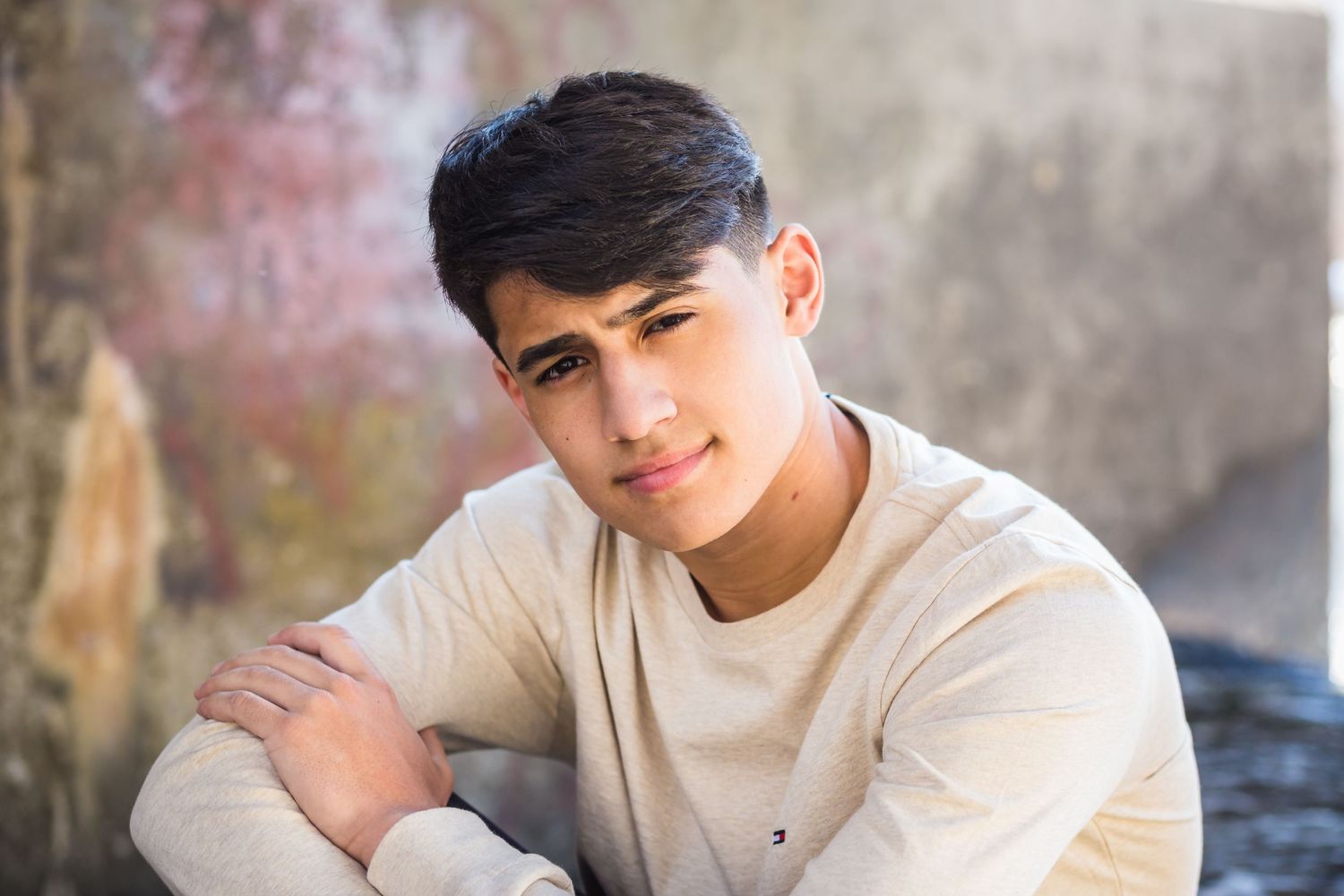 Portrait of person in beige sweater against textured wall background.