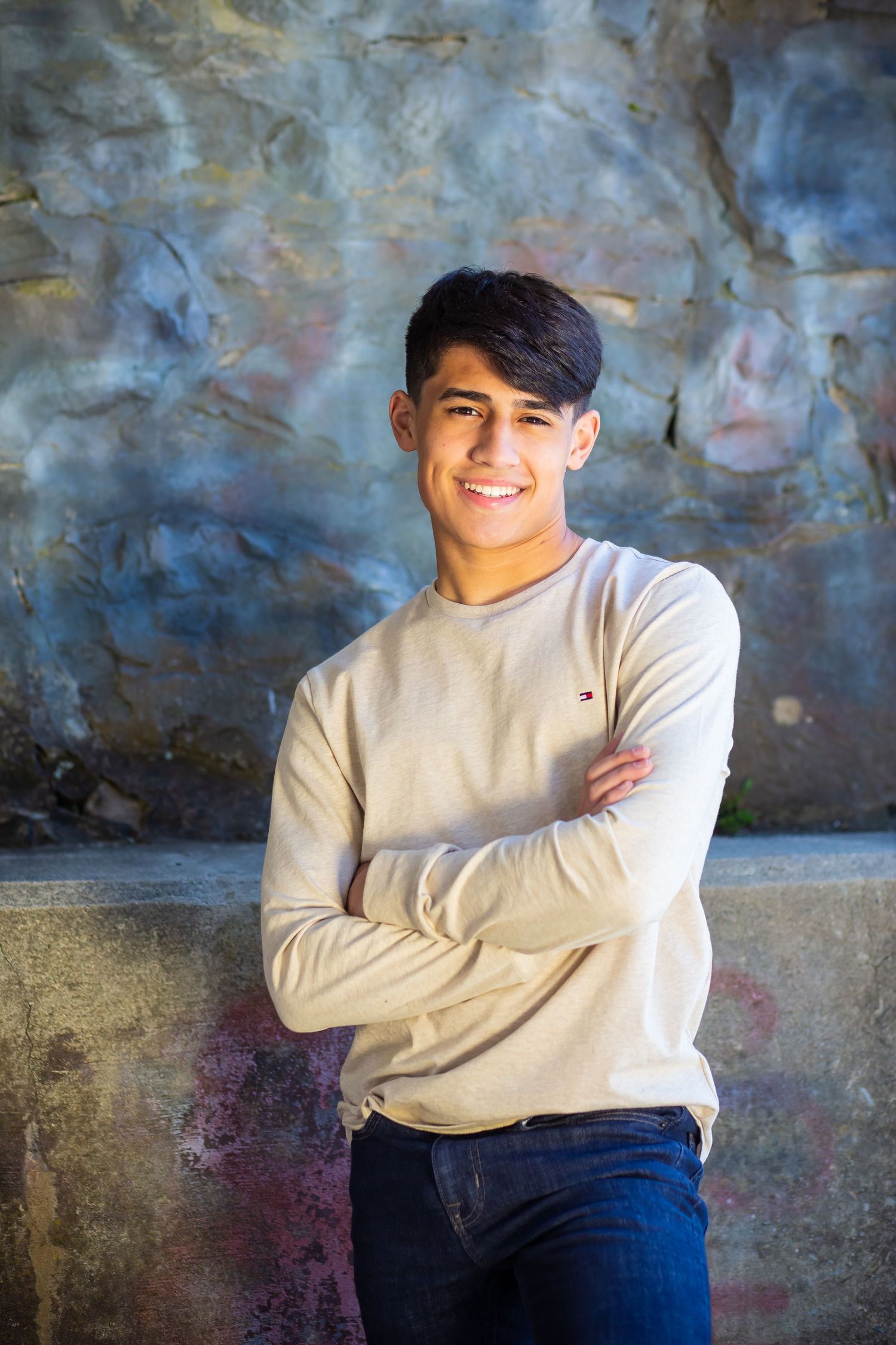 Portrait of a young person in a beige sweater smiling against a textured blue wall background.
