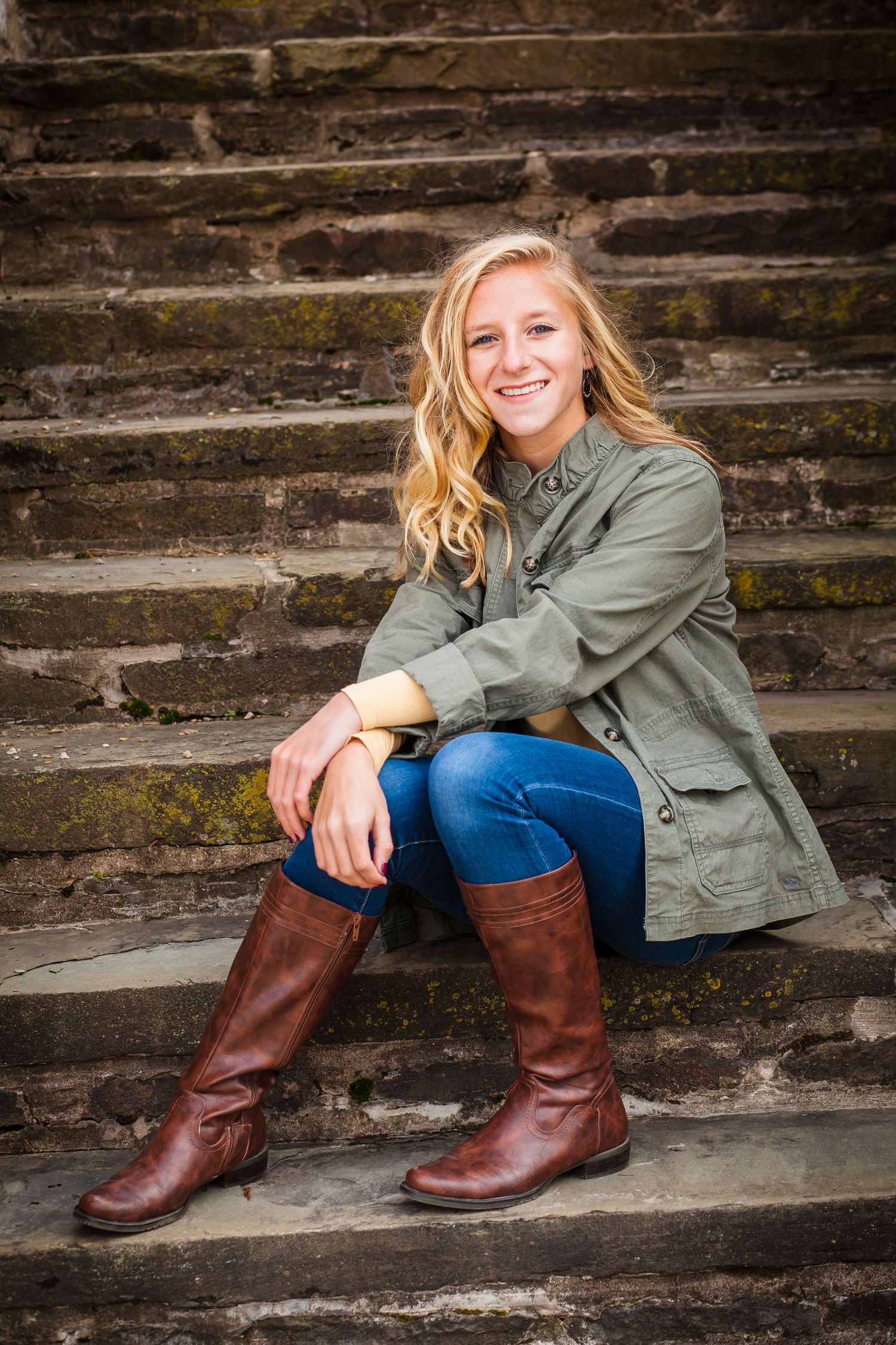 A casual outdoor portrait on stone steps wearing brown boots and an olive jacket.