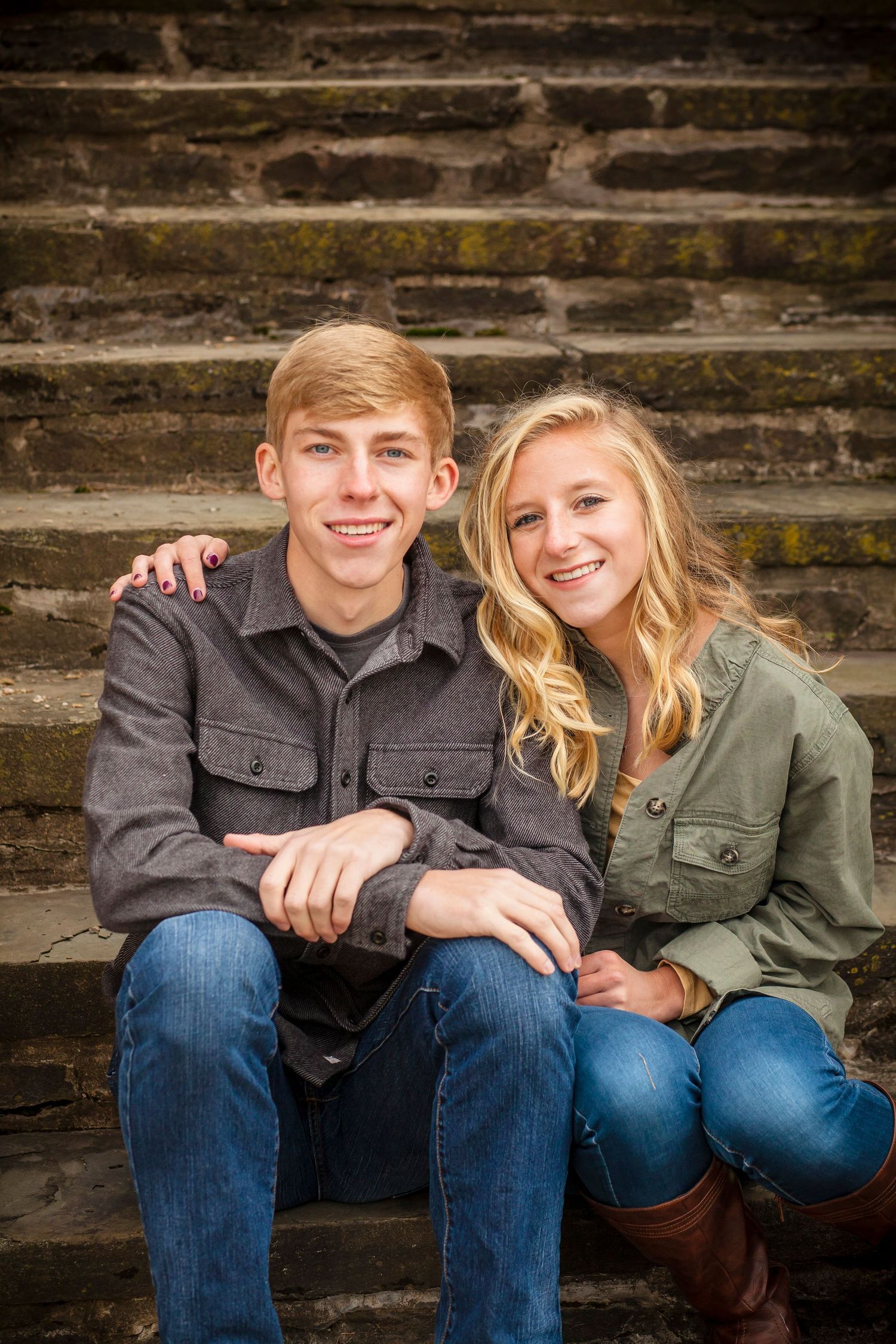 A couple sitting together on stone steps wearing matching olive jackets.