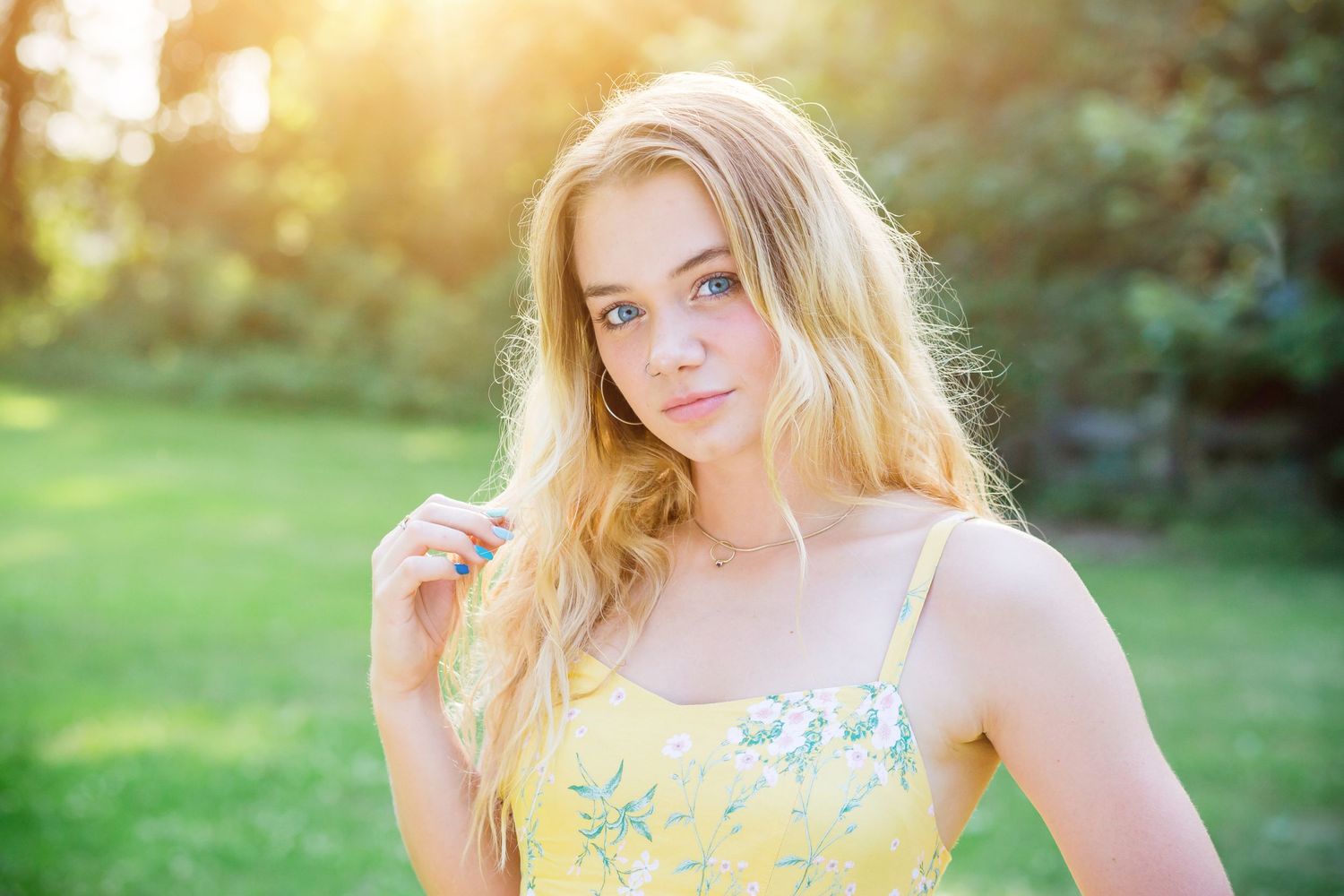 Outdoor portrait of a blonde person in a yellow floral dress with sunlit natural background.