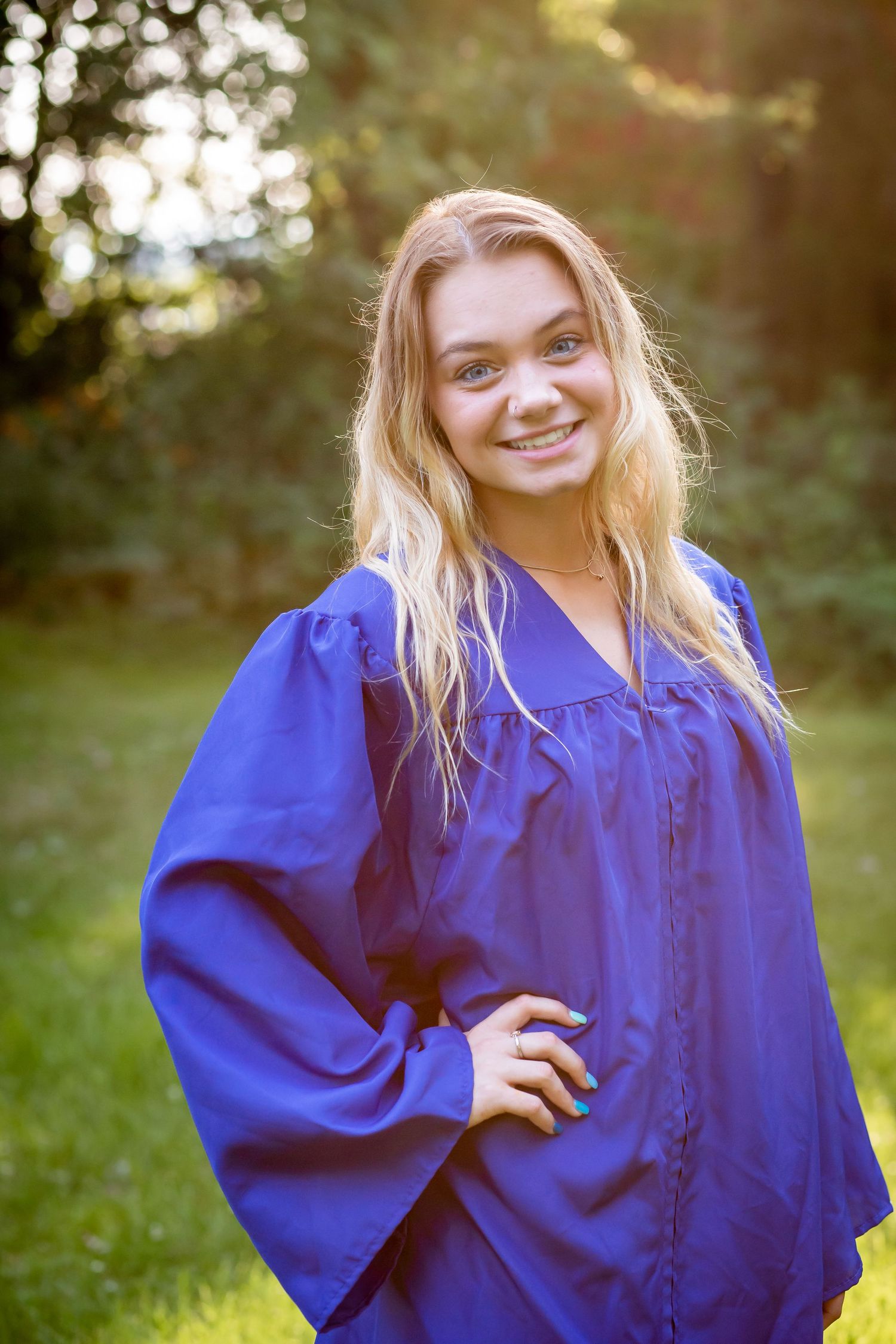 Graduate in royal blue graduation gown poses outdoors with natural background.