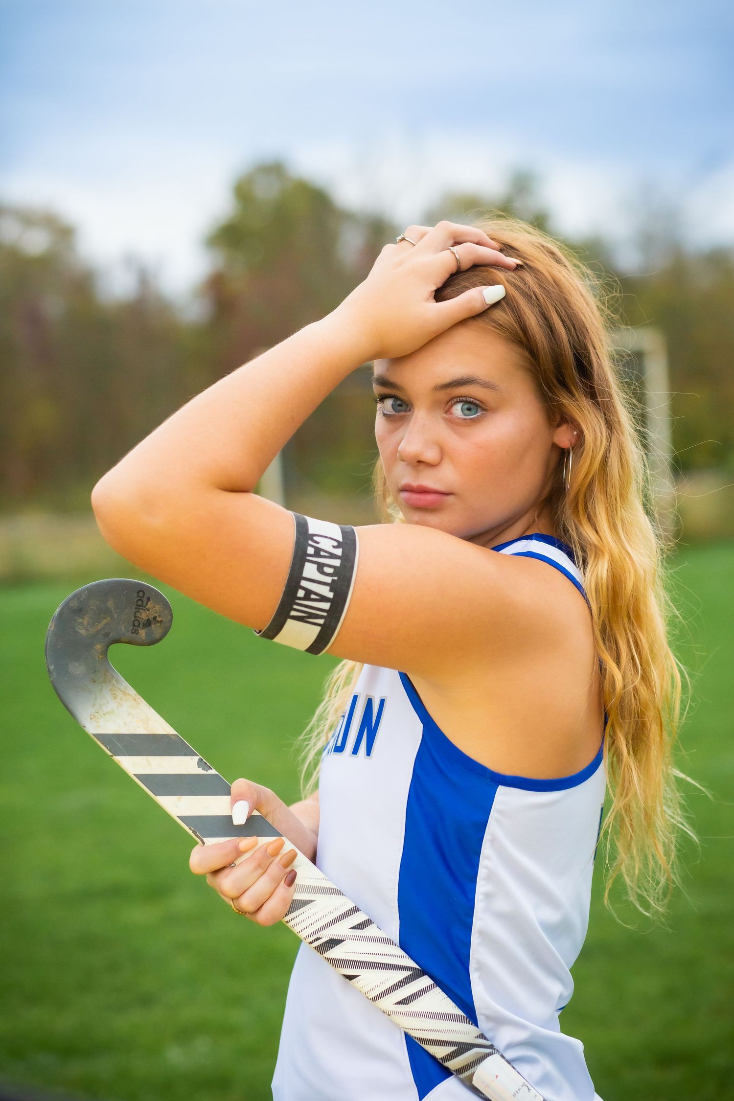 Athletic portrait with field hockey stick and blue sports uniform in outdoor setting.