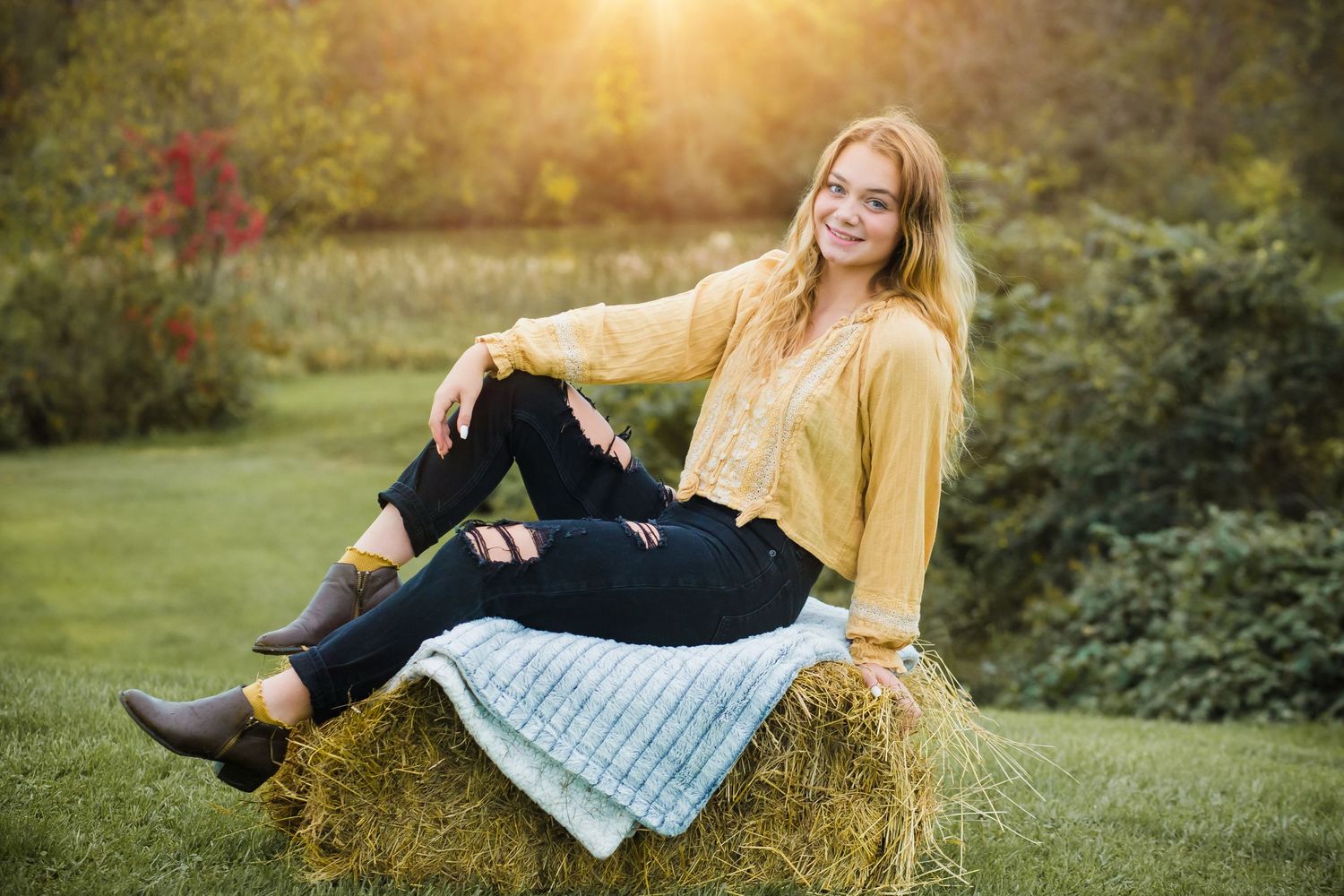 Casual autumn portrait on hay bale wearing yellow cardigan and boots at sunset.