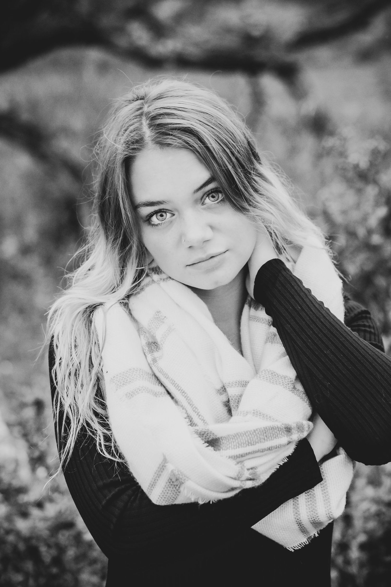 Black and white portrait with plaid scarf and dark sweater against blurred background.