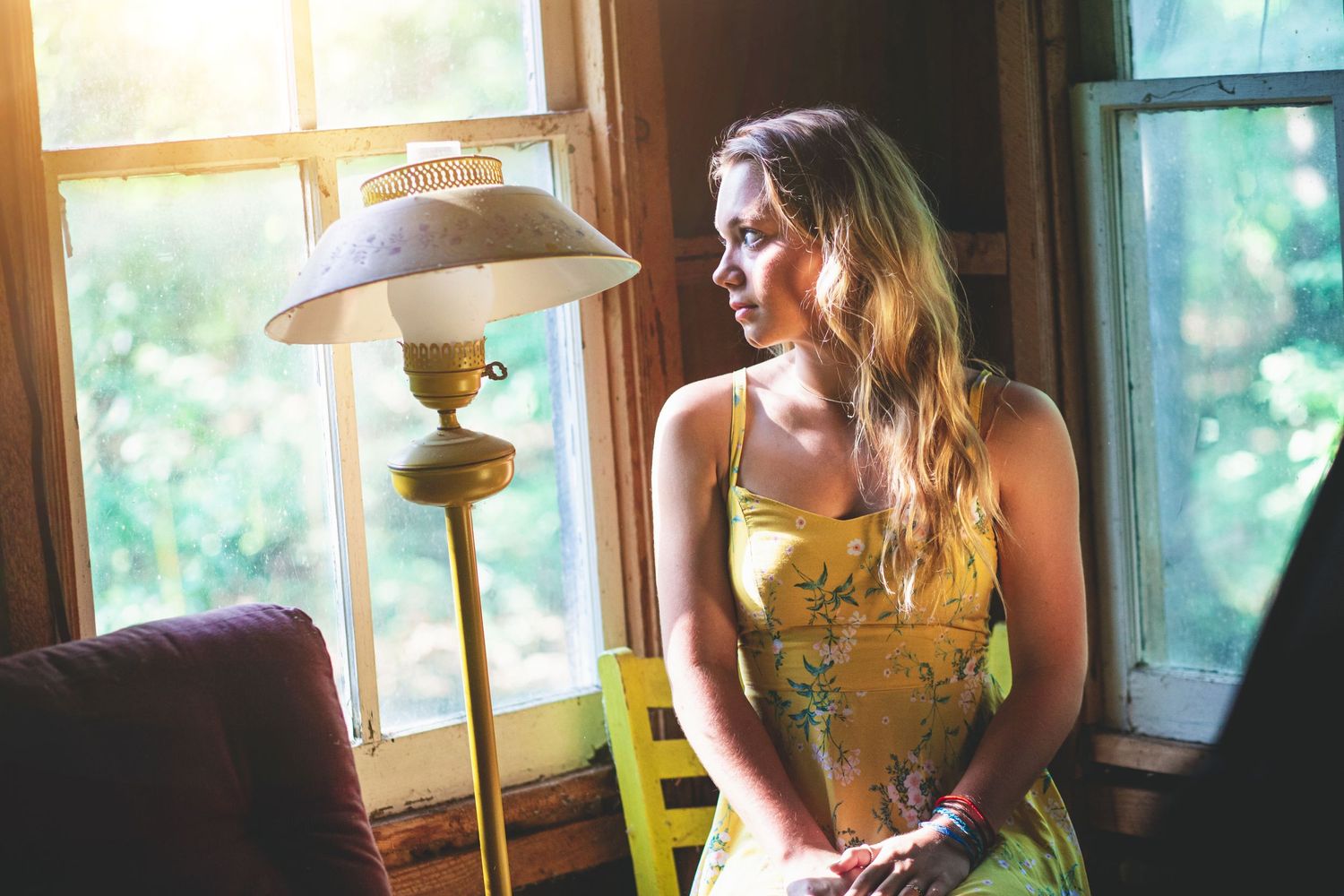 Indoor portrait near window with vintage lamp showing person in yellow dress with soft lighting.