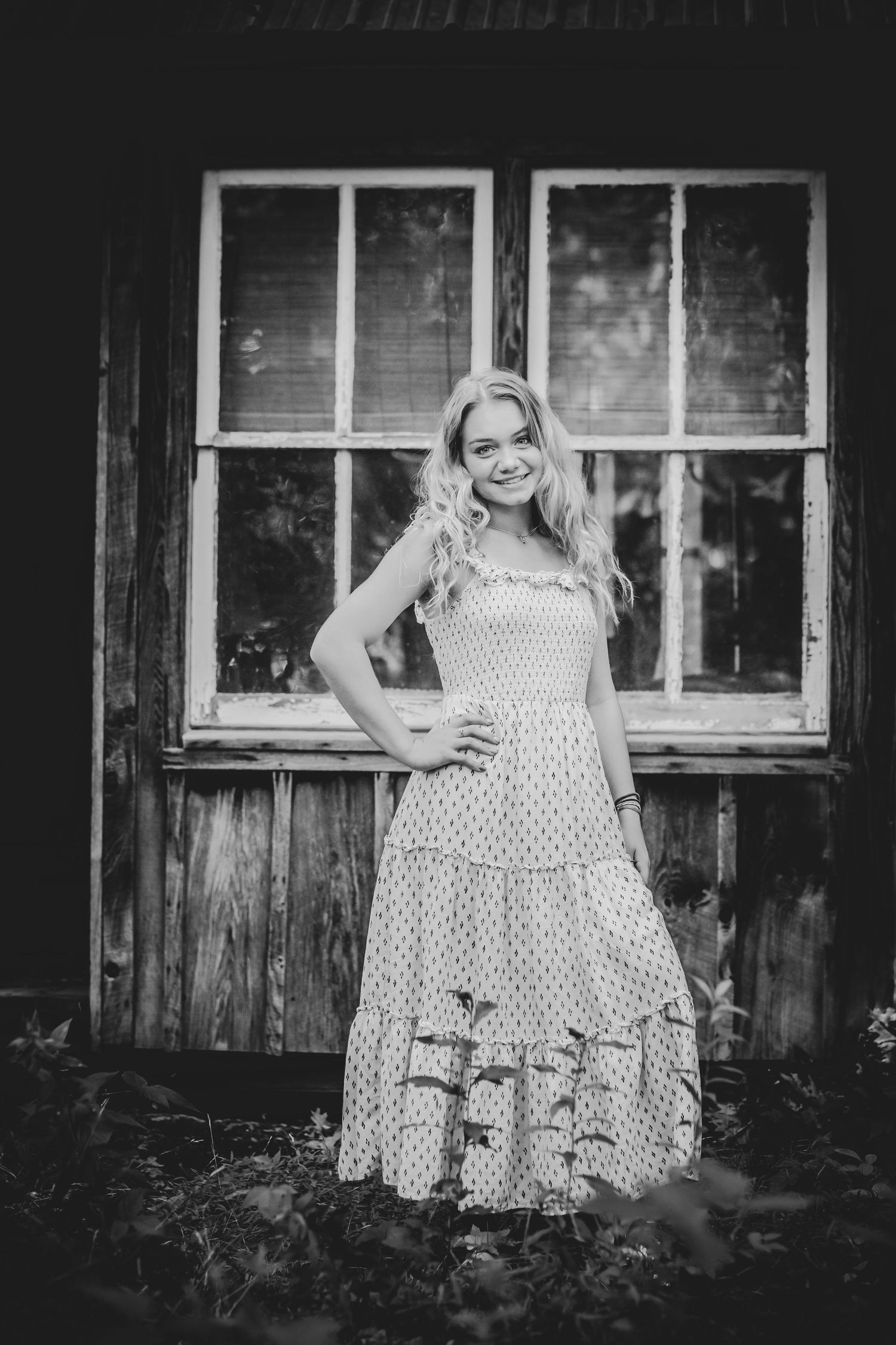 Black and white portrait of person in polka dot dress against rustic wooden wall.