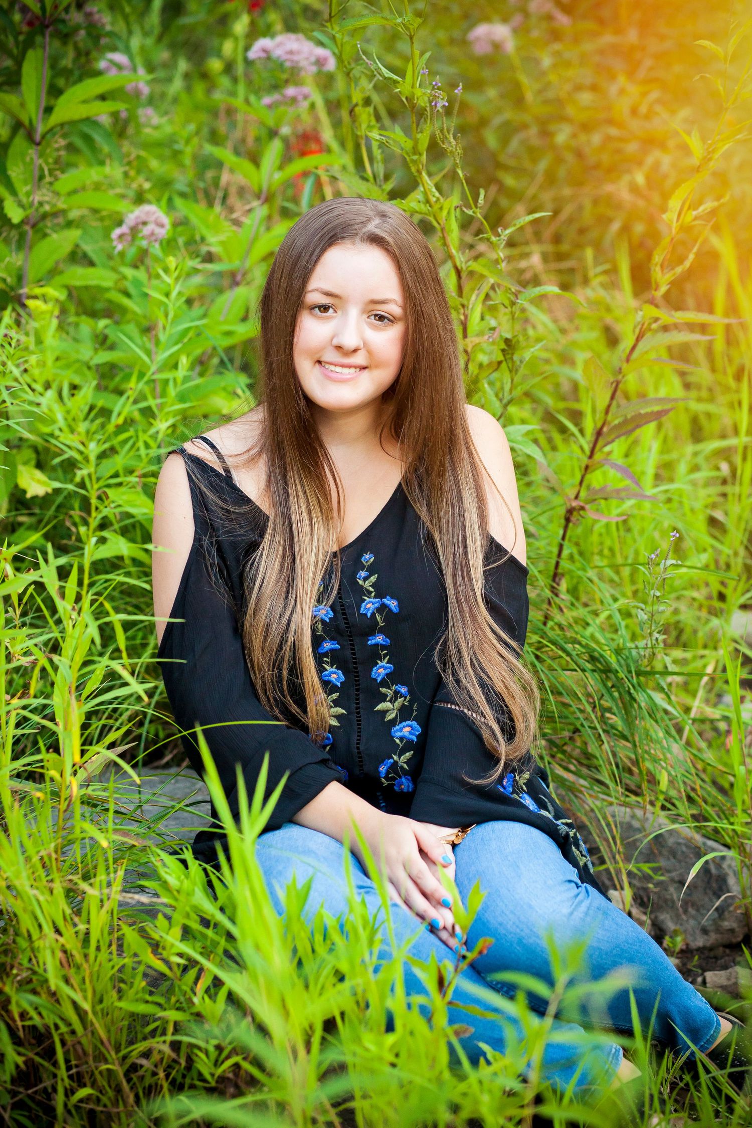 A summer portrait in a garden wearing a black floral top among green plants.