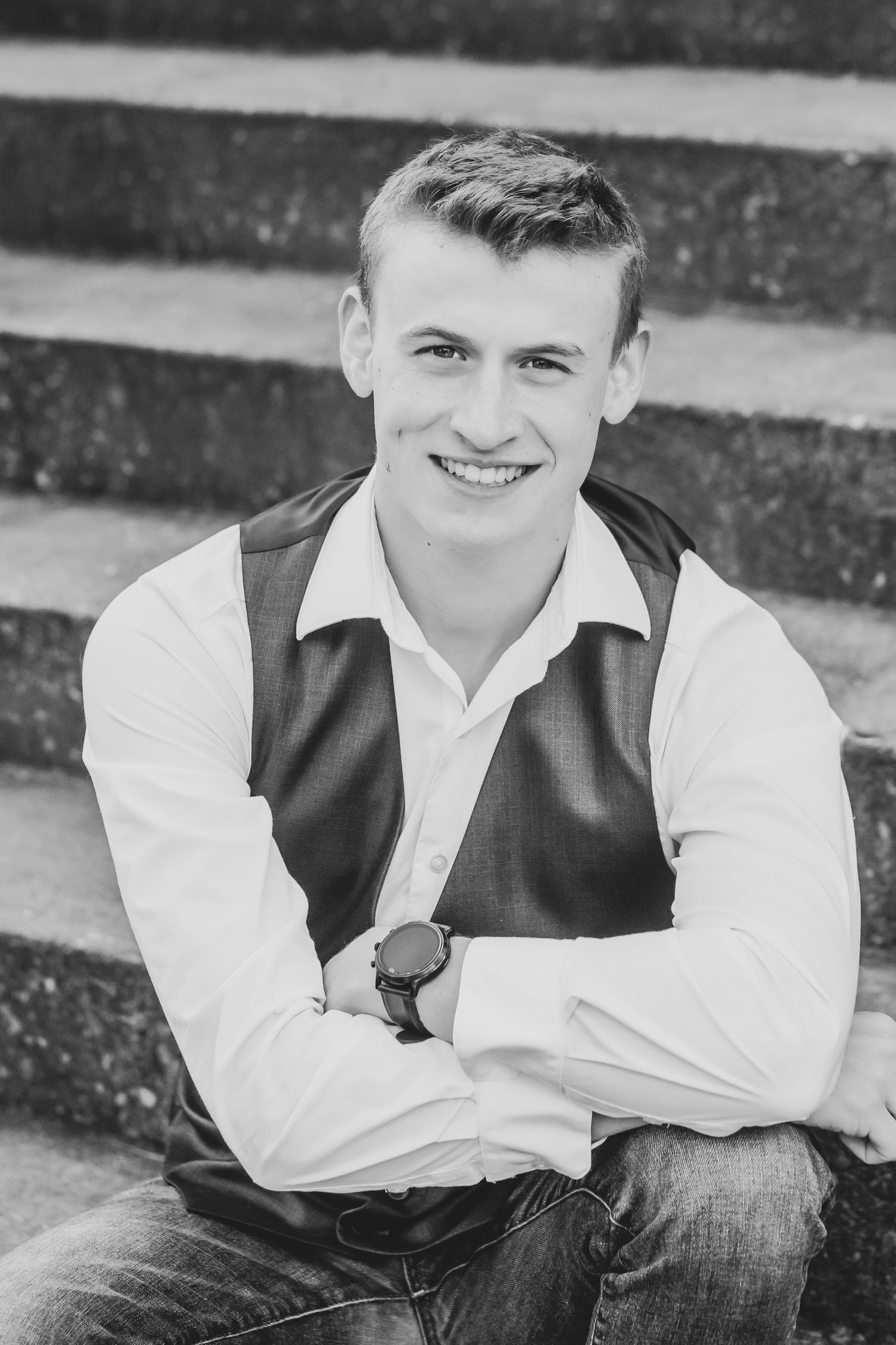 Black and white portrait on stone steps wearing vest and dress shirt with classic styling.