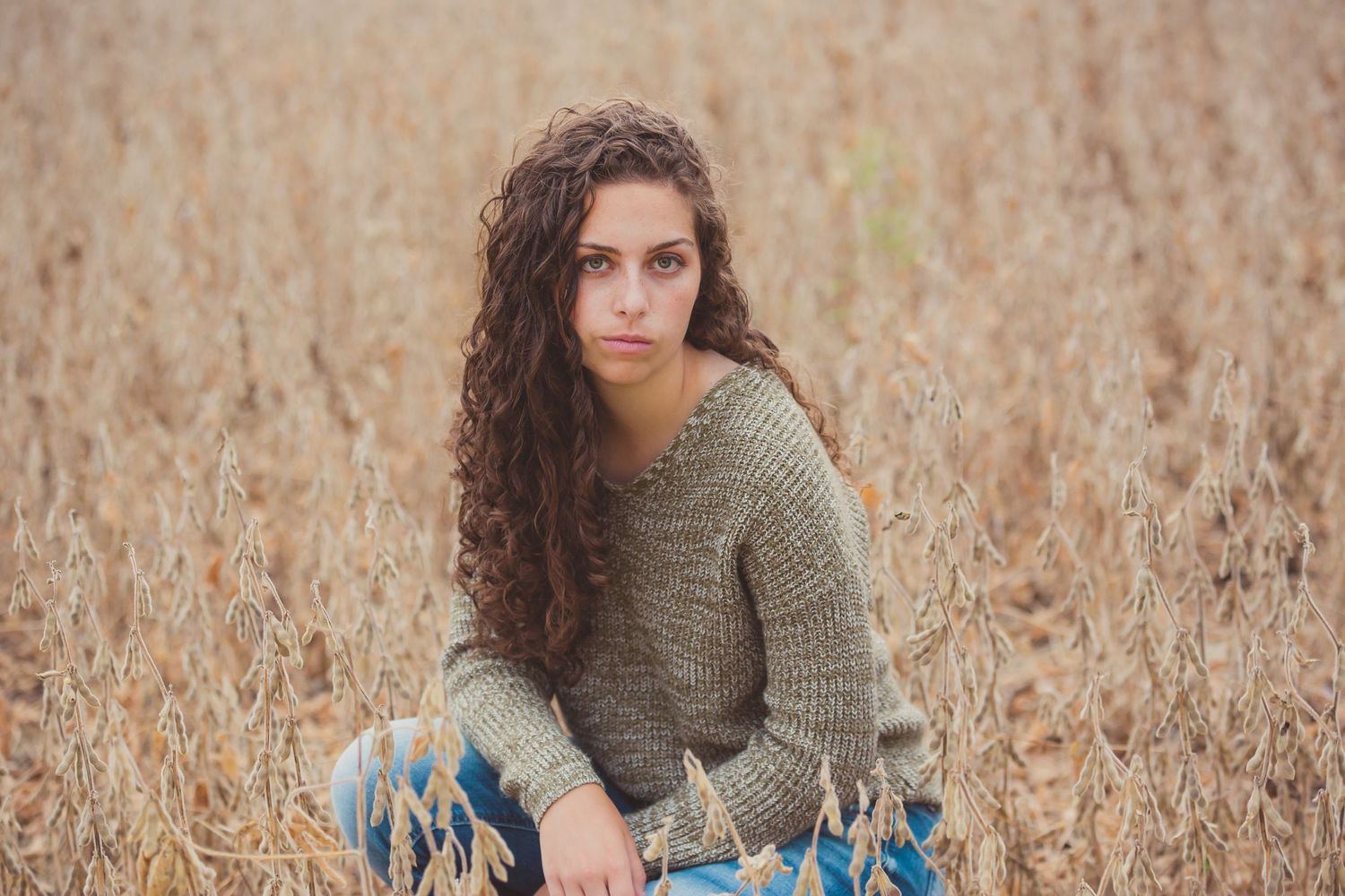 Artistic portrait in wheat field with person wearing olive sweater in muted tones.