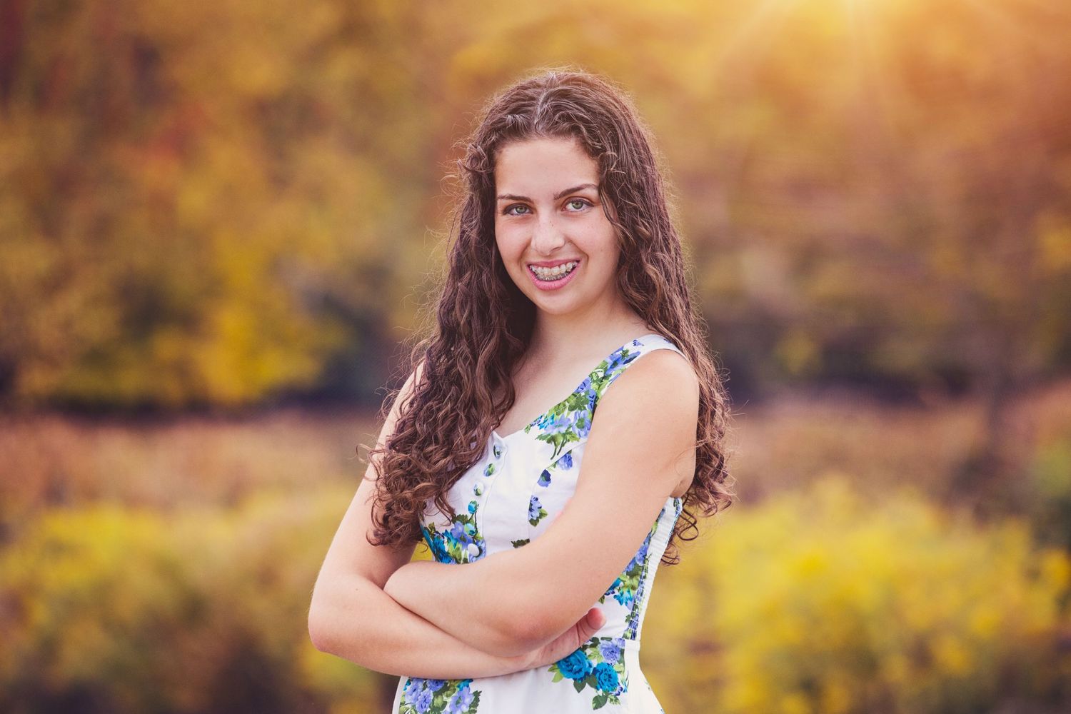 Portrait of someone in floral dress against autumn foliage backdrop at sunset.