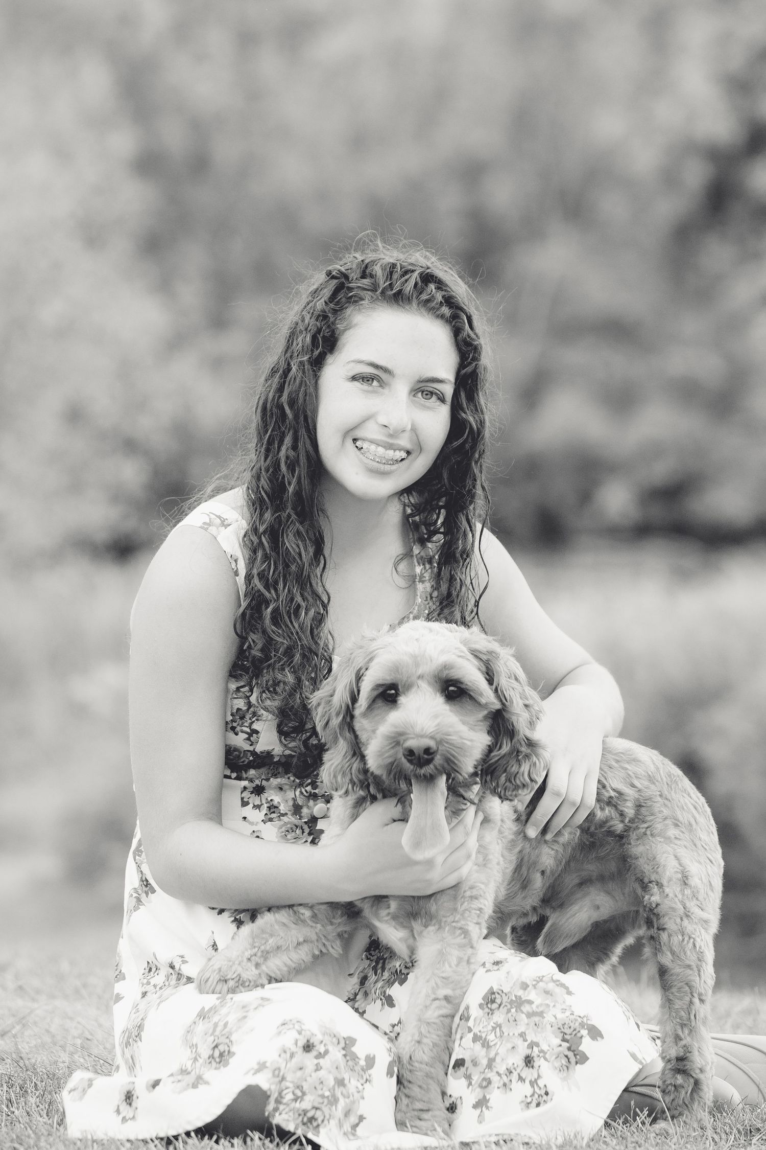 Black and white portrait with curly-haired person holding friendly fluffy dog outdoors.