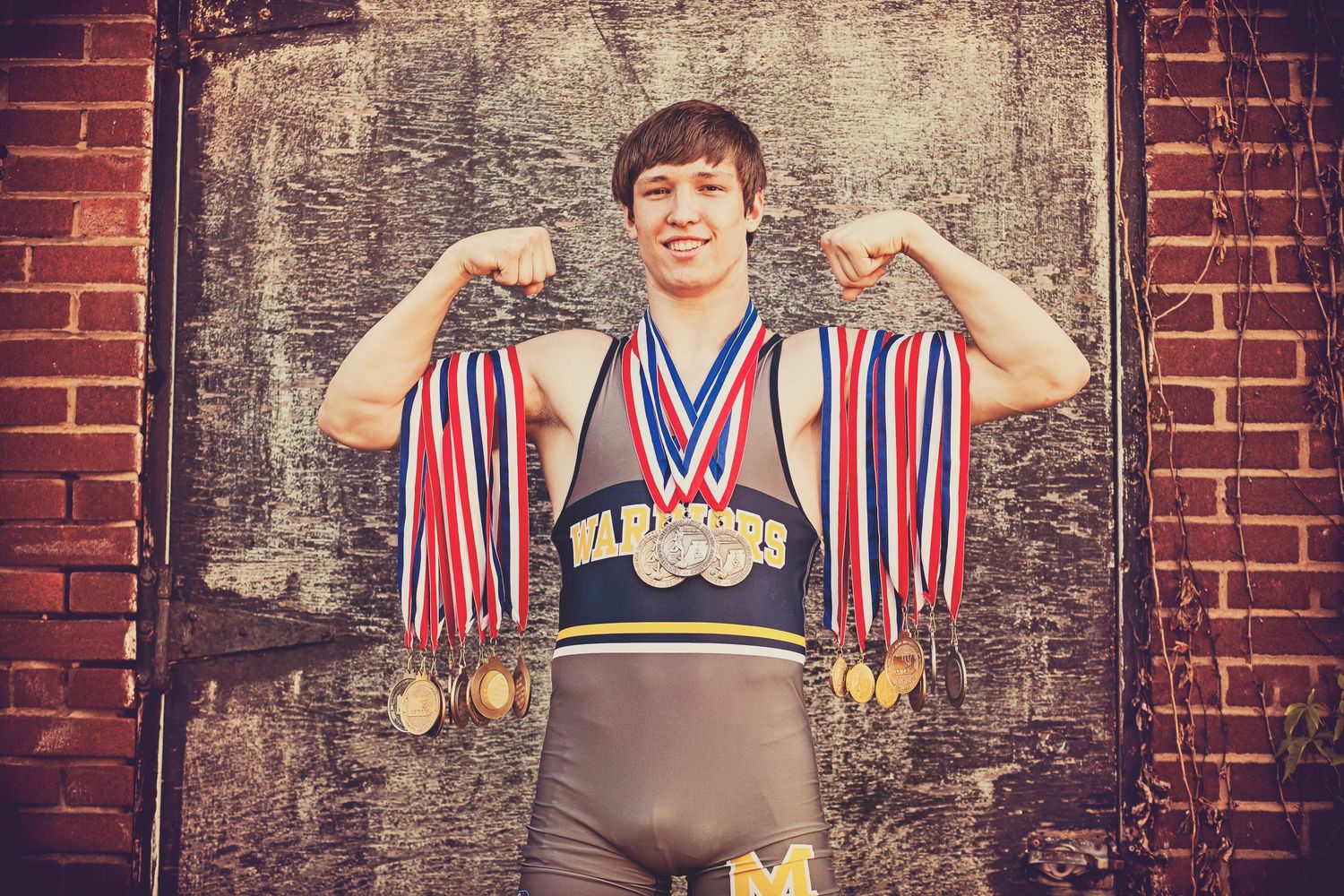 An athlete displaying multiple medals wearing a striped jersey against a brick wall.