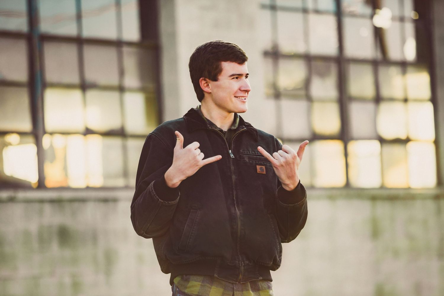 A casual portrait showing hand gestures against an industrial window background.