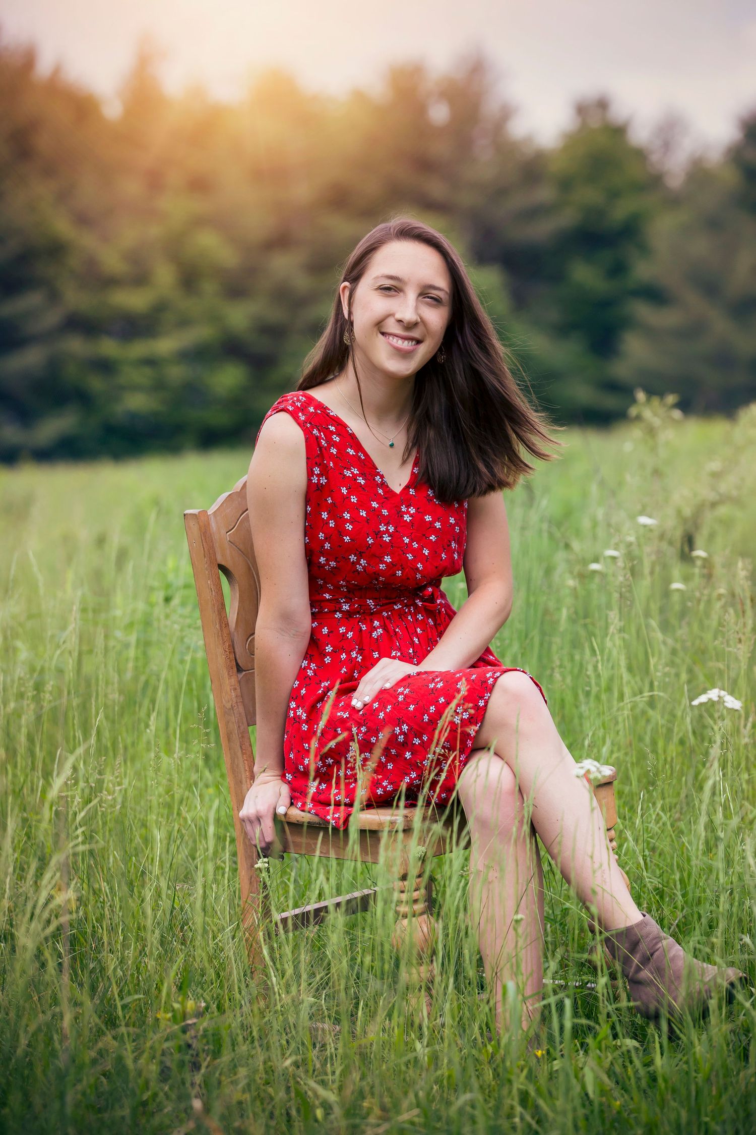 Person in a red polka dot dress sits on a wooden chair in a sunny summer meadow.