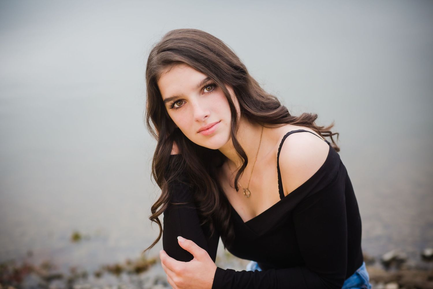 Portrait of a woman wearing a black off-shoulder sweater against a soft gray background.