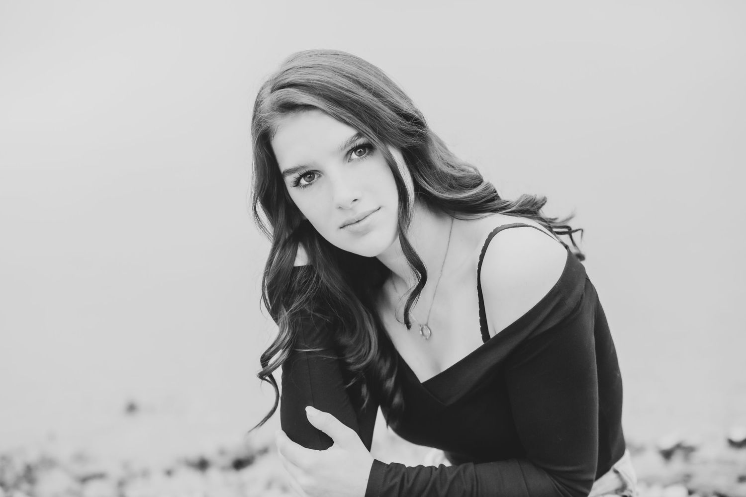 Black and white portrait of a woman in an off-shoulder sweater with flowing dark hair against a light background.
