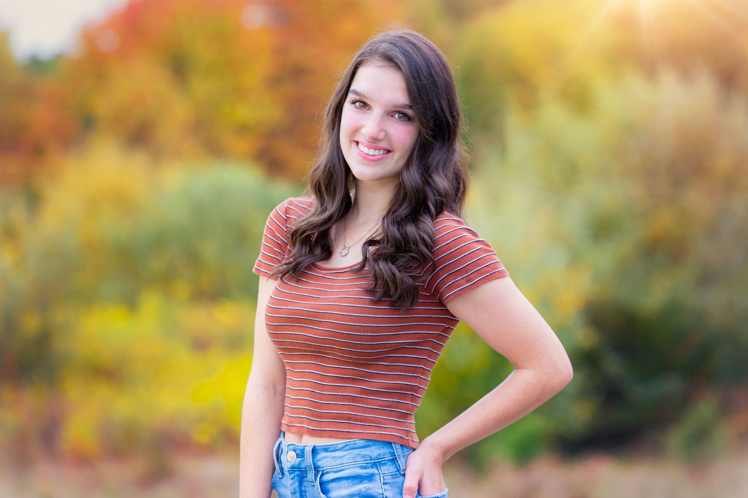 Autumn portrait of a person in a striped top and denim against colorful fall foliage.