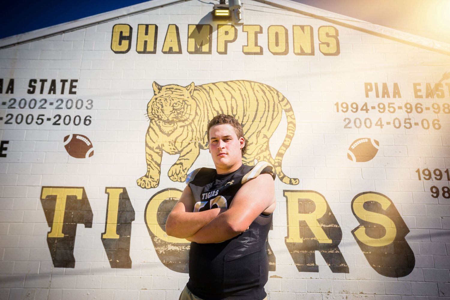 Athletic figure poses in front of a champions wall with tiger mascot and football decorations.