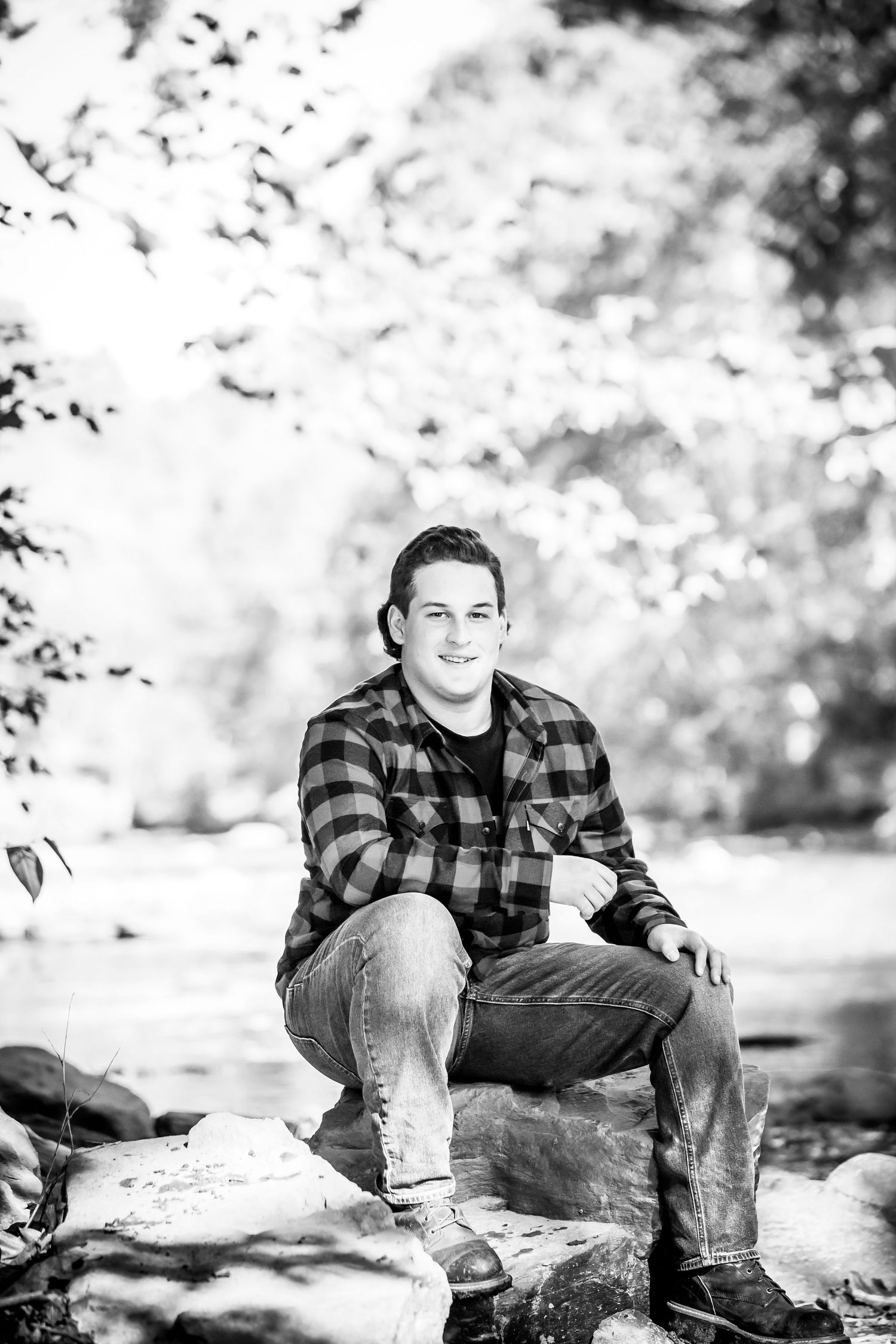 Black and white portrait on rocky terrain wearing plaid flannel and jeans in natural setting.