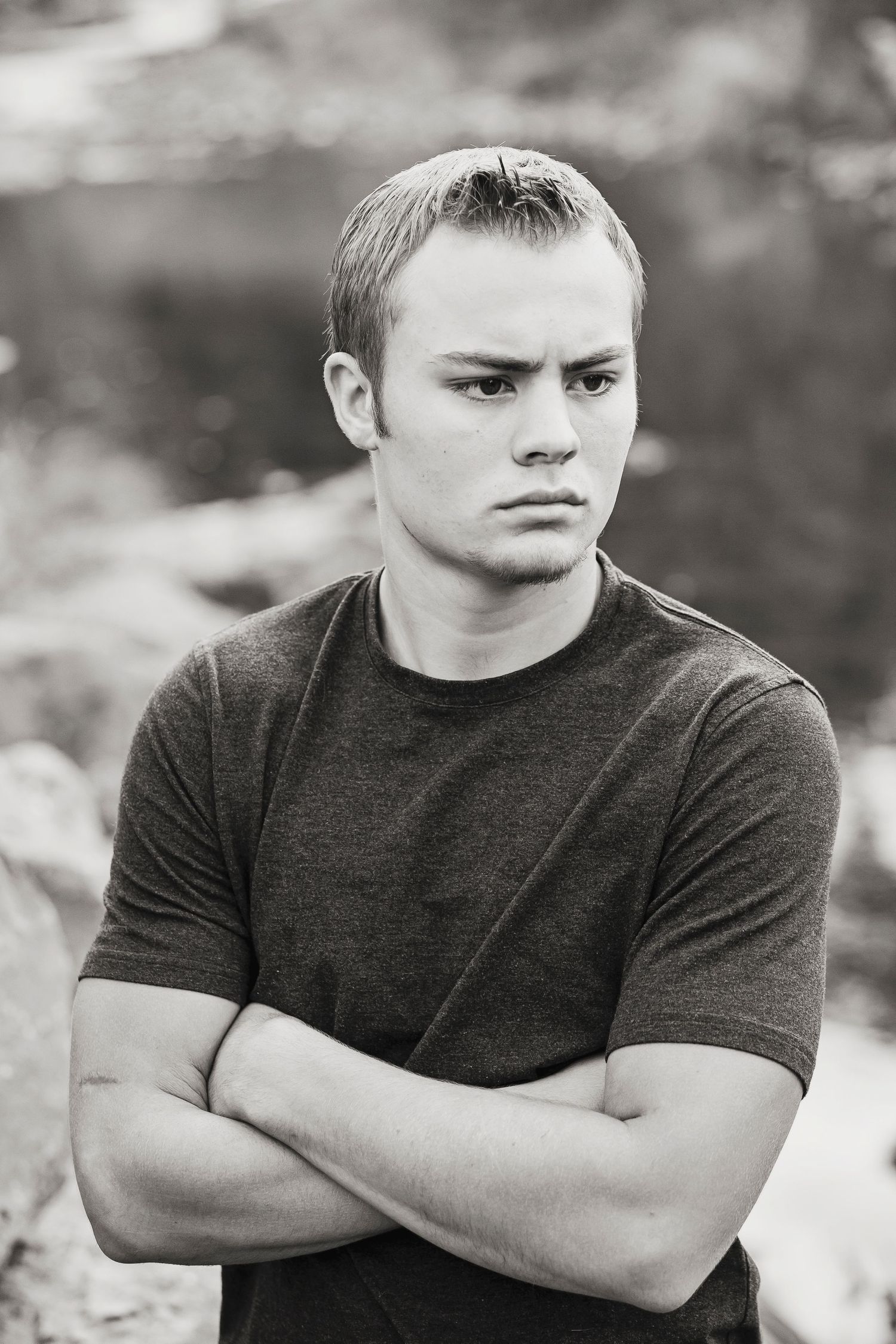 Black and white portrait against blurred background showing serious expression and crossed arms.