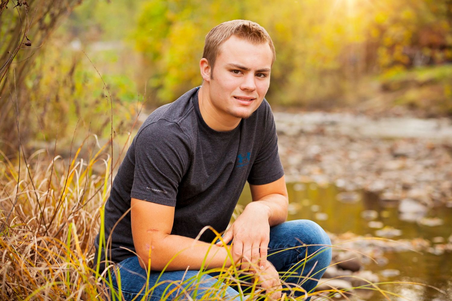 Casual outdoor portrait by stream with autumn foliage and golden sunlight.