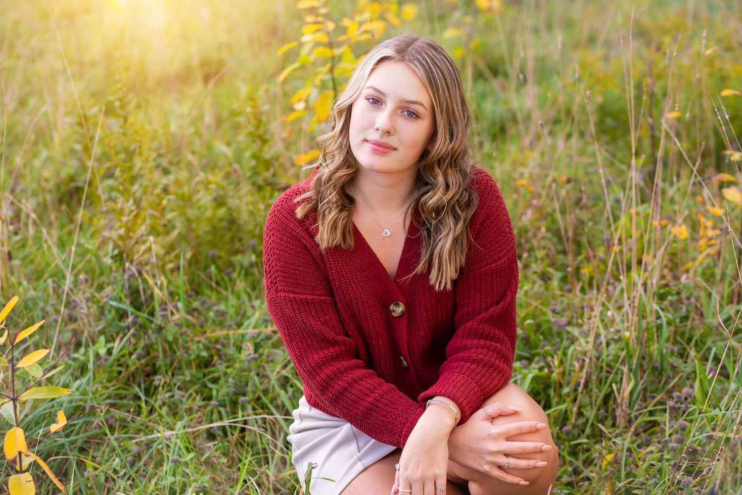A casual outdoor portrait in a red sweater amid autumn wildflowers at golden hour.