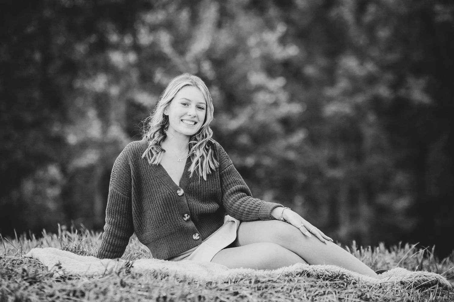 A black and white outdoor portrait on grassy ground with soft bokeh background.