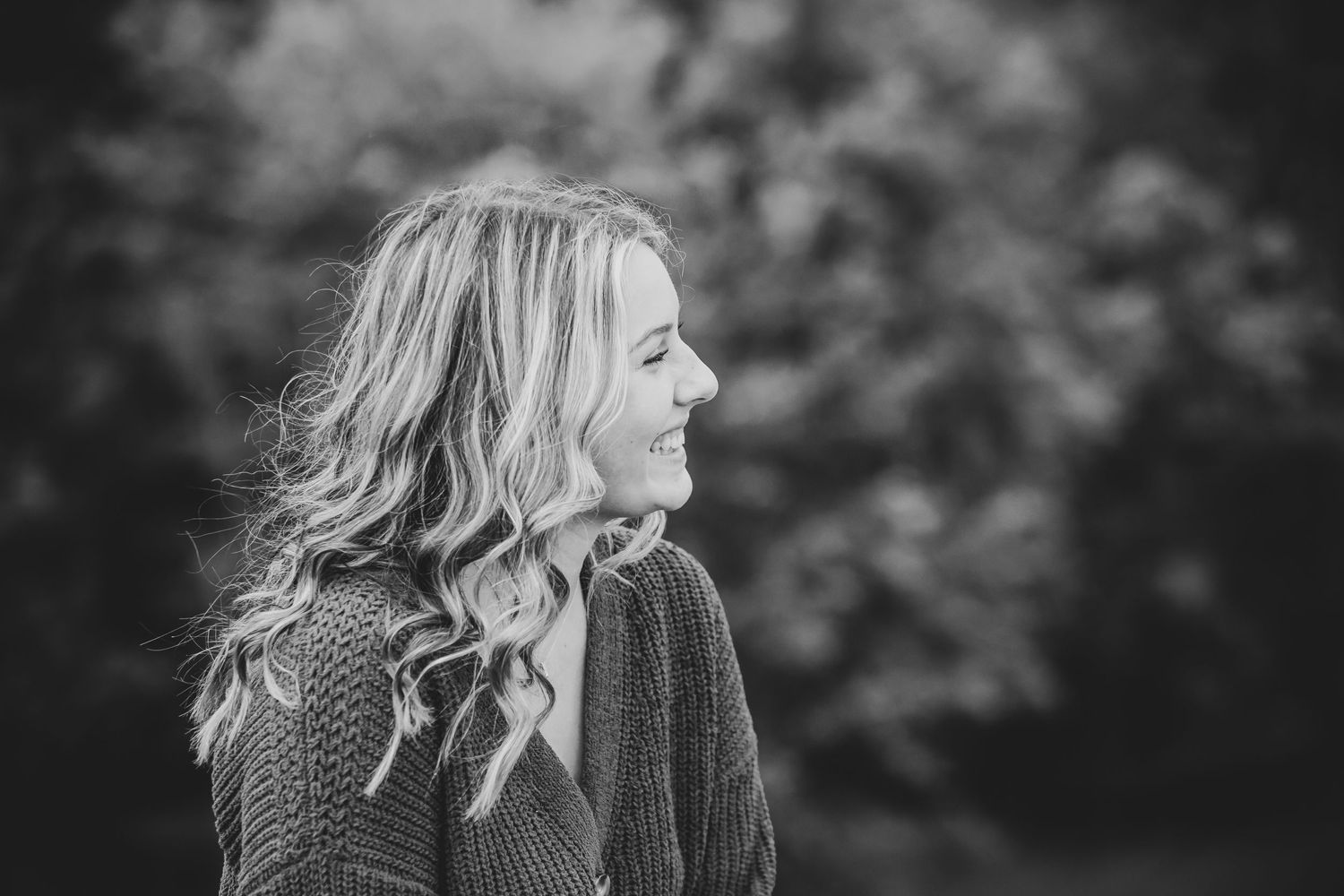 Black and white portrait in a sweater with natural outdoor background and soft lighting.