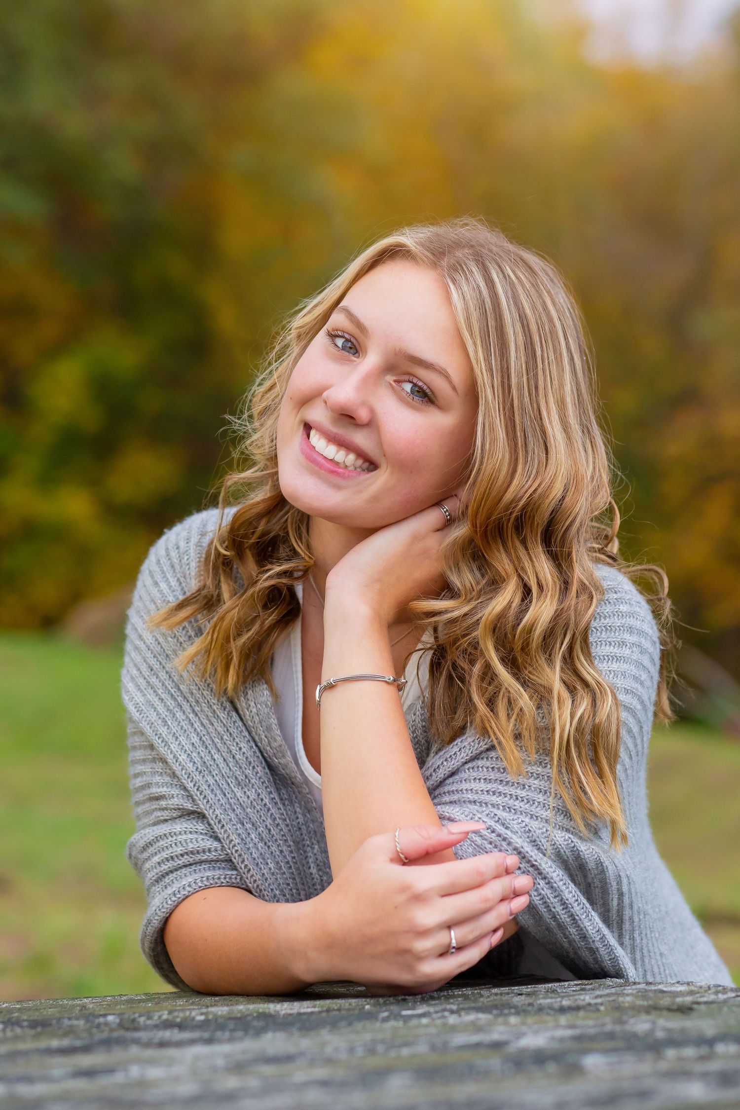 Casual portrait leaning on wooden surface with autumn foliage in background.