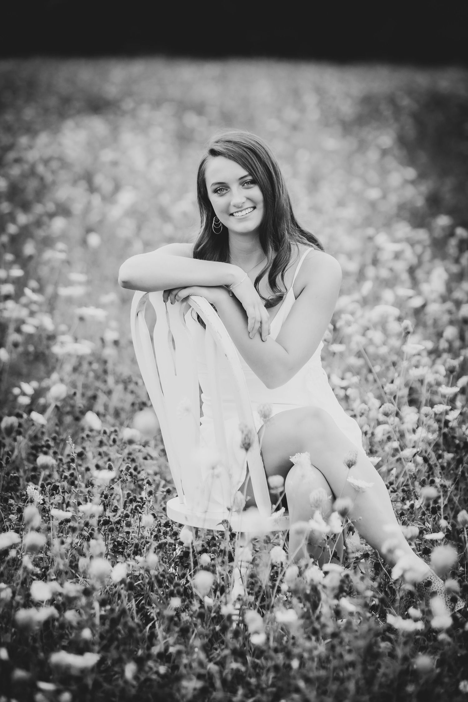 Black and white portrait sitting in a flower field with vintage chair.