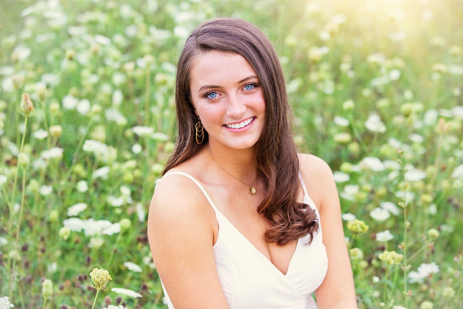 Summer portrait in white top with daisy wildflowers and warm sunlight.