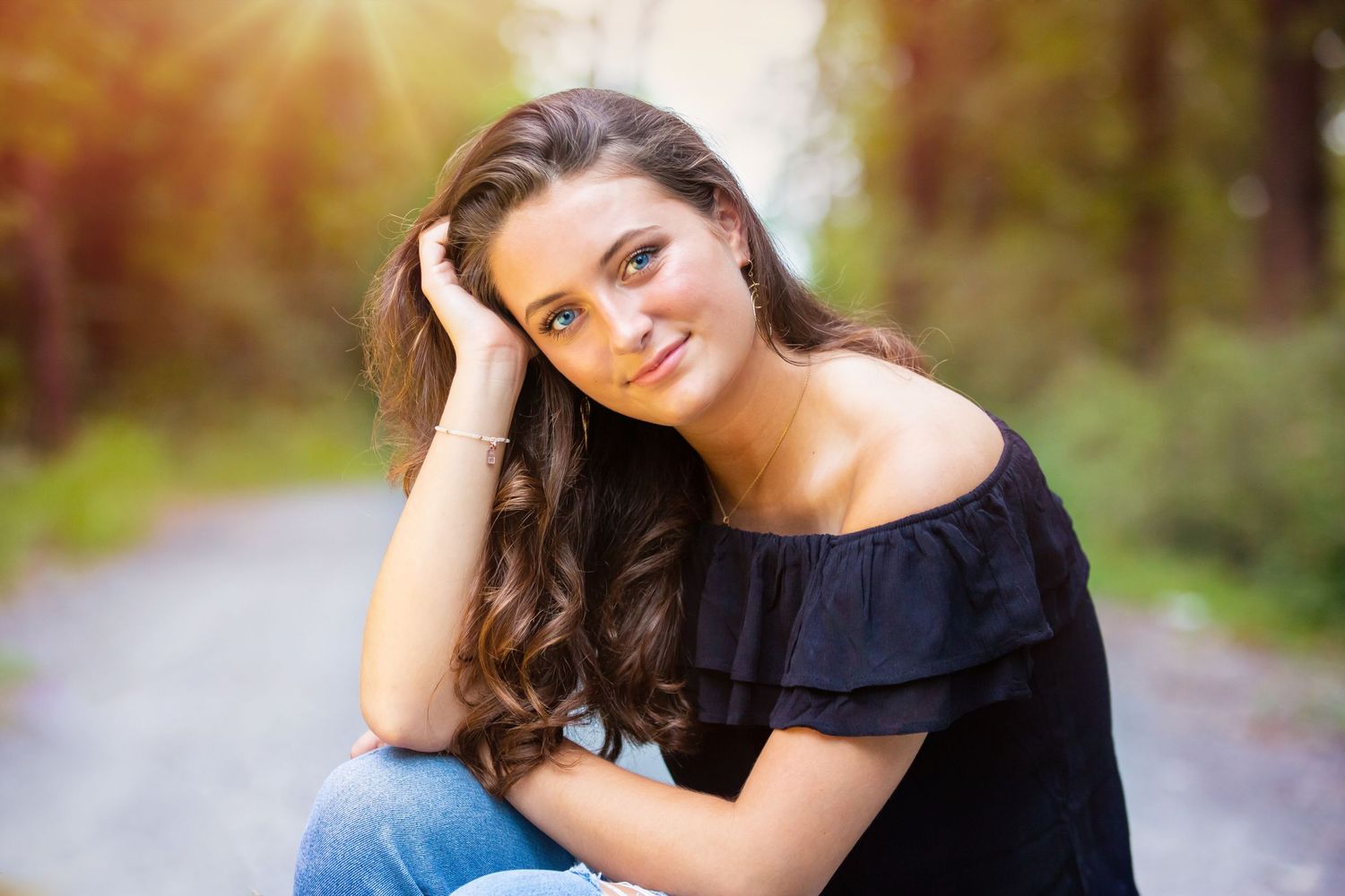 Portrait in natural lighting with off-shoulder black top and long wavy hair on a forest path.