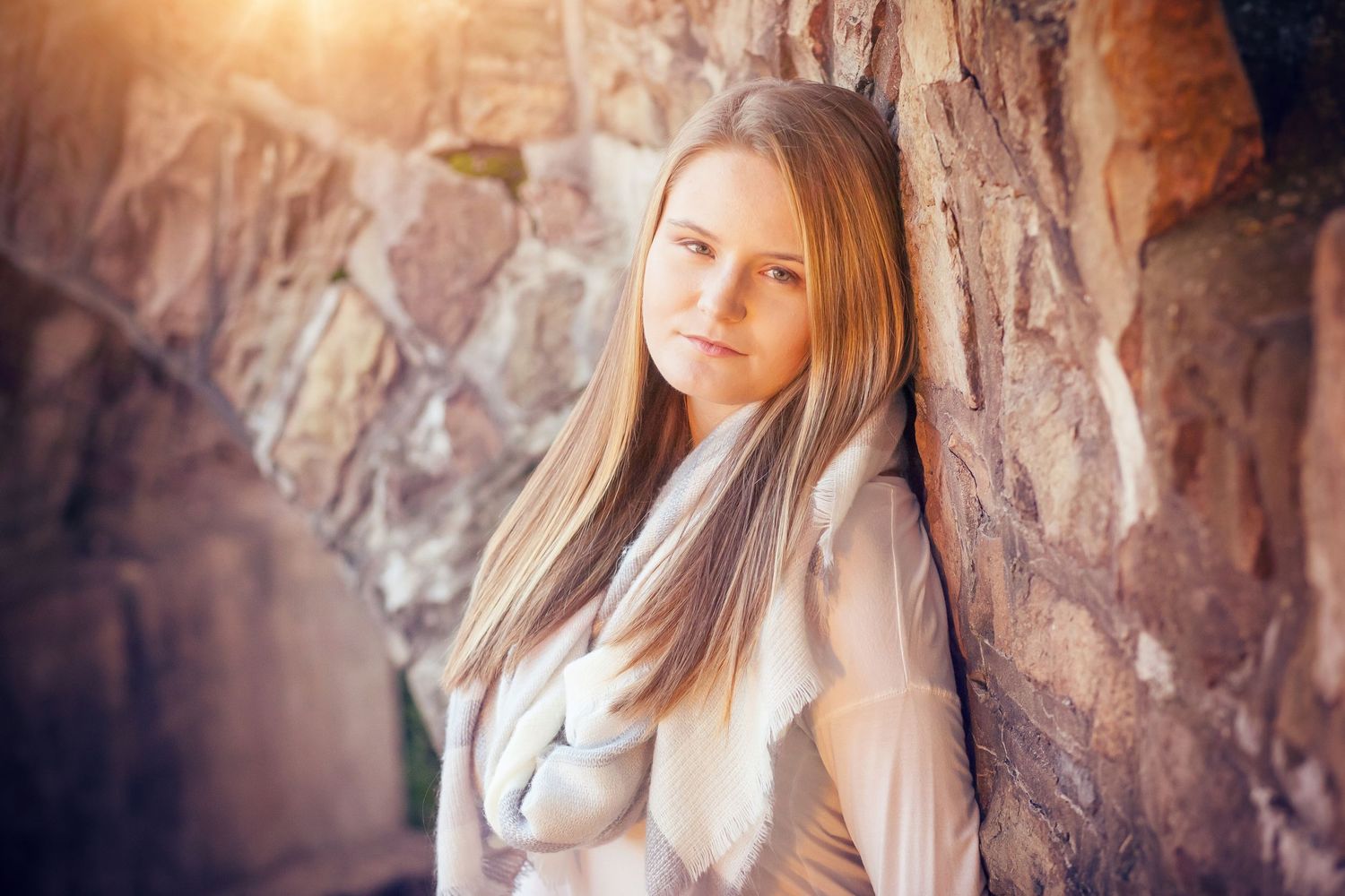 Portrait against stone wall wearing light colored sweater with long straight hair.