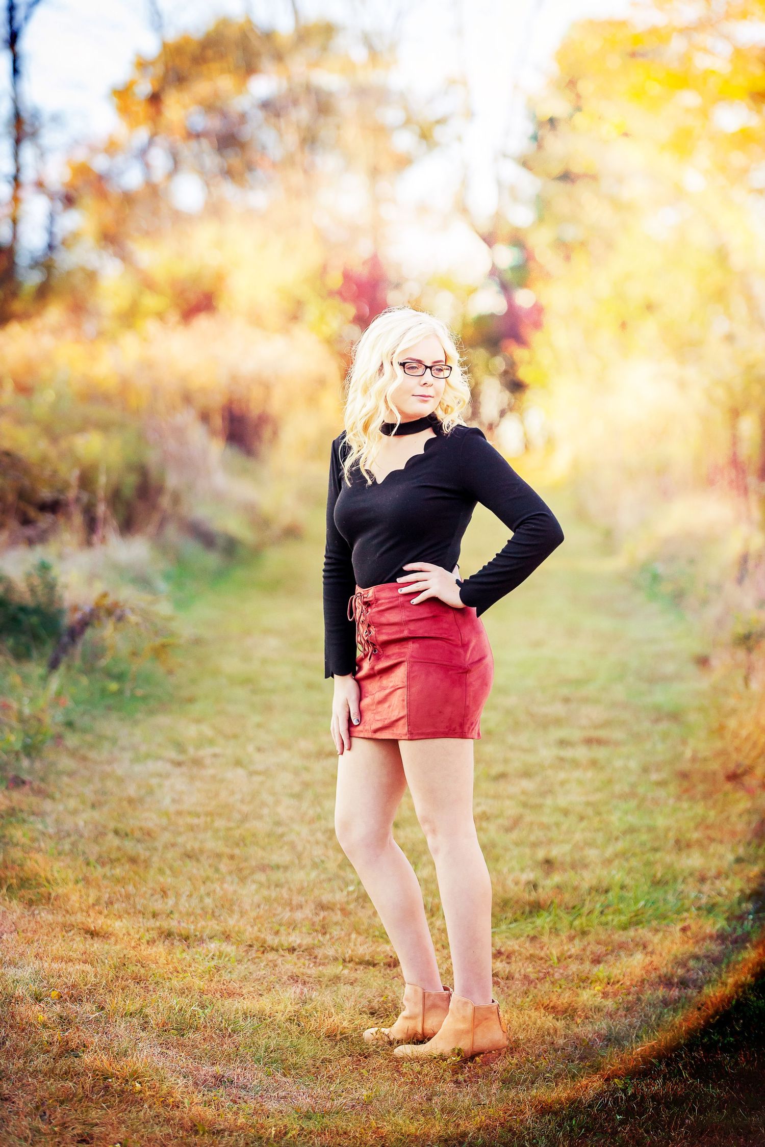 Fashionable autumn outfit featuring red shorts and black top on a sunlit nature path.