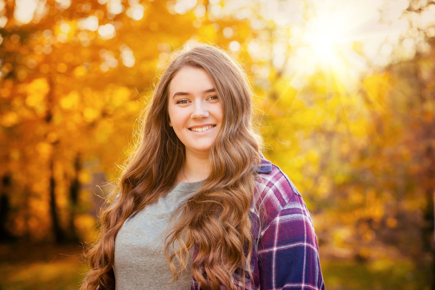 Autumn portrait with plaid shirt and gray top against golden fall foliage background.